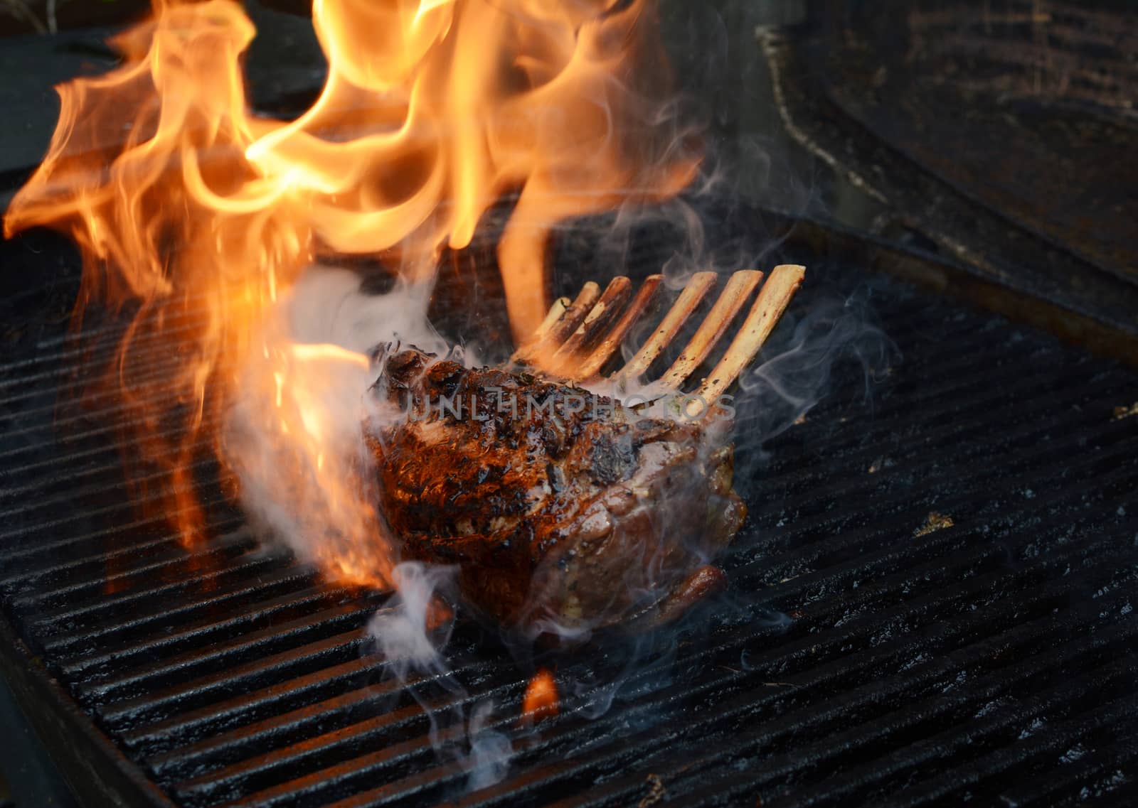 Tender rack of lamb being grilled, with large flames and smoke rising from the barbecue
