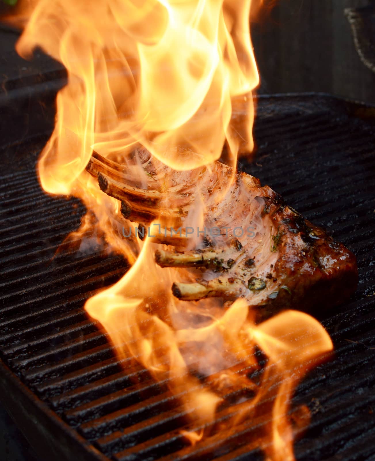 Hot flames engulf grilled meat - a rack of British lamb with 7 ribs on a barbecue