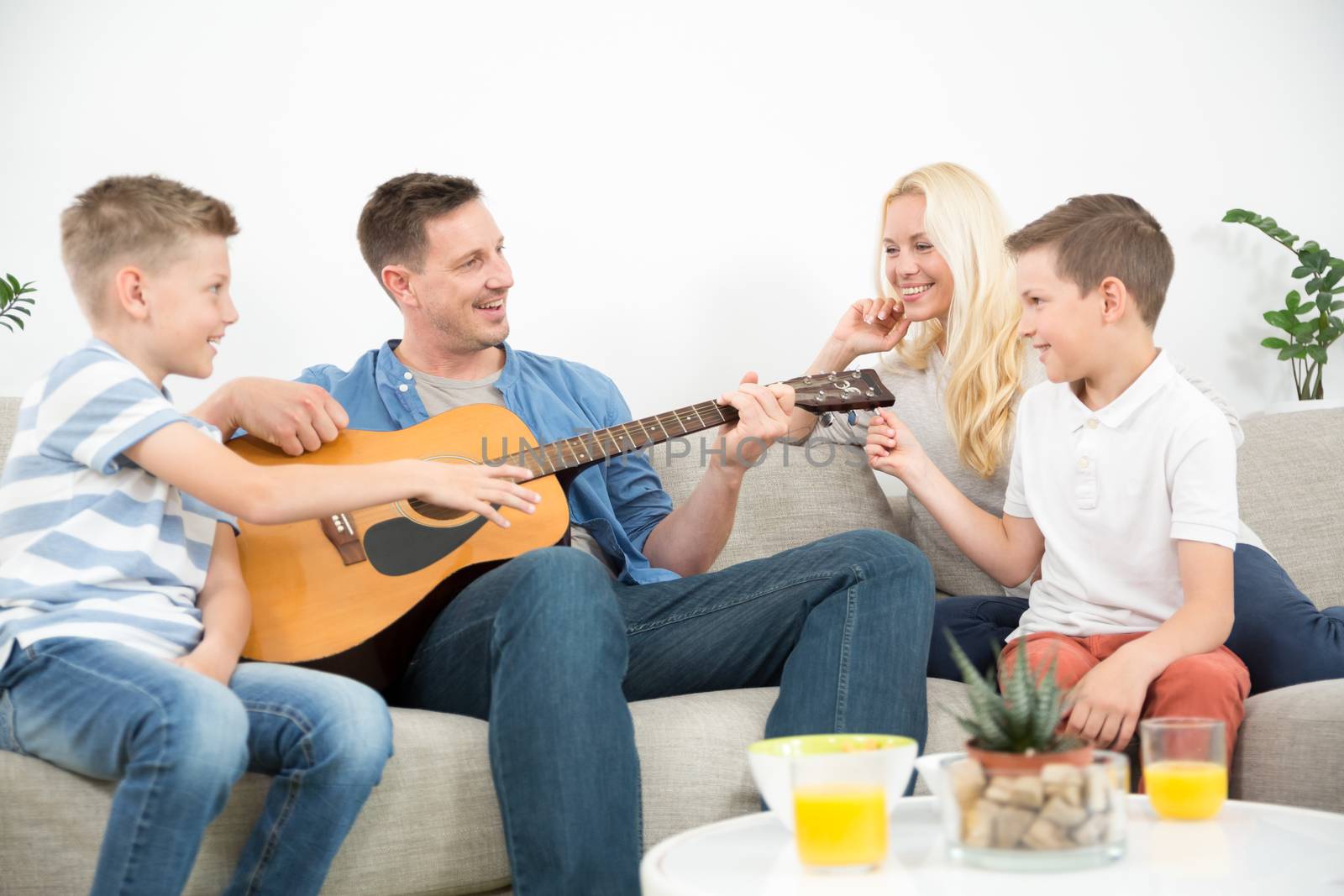 Happy caucasian family smiling, playing guitar and singing songs together at cosy modern home by kasto