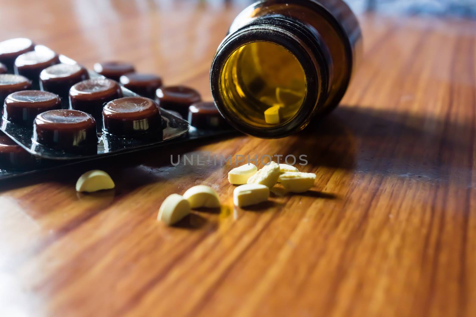 Close up Open transparent glass bottle with medicine pills or tablets blister pack on wooden table background. Pharmacy cure and health concept. Selective focus shallow depth of field. Natural Light.