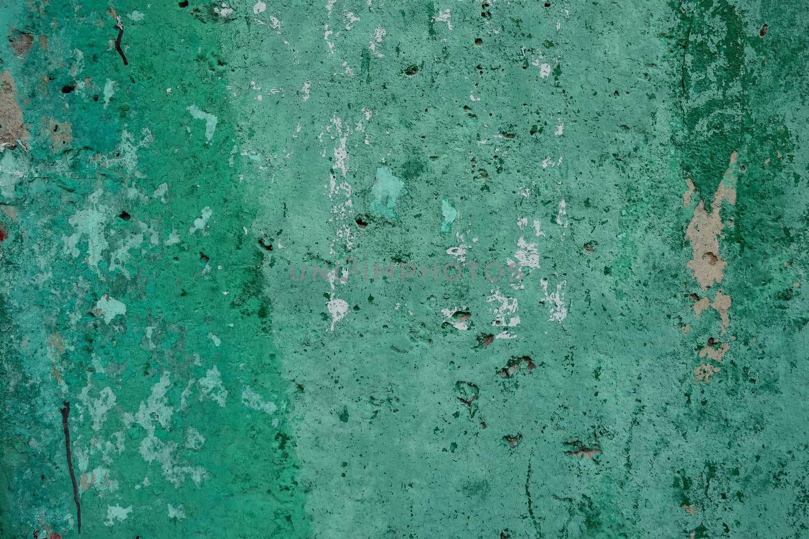 Background of green textured shabby wall with stains of paint and holes in daylight. Close-up. Copy space