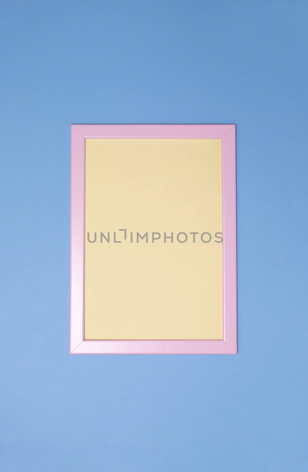 Empty pink photoframe with yellow paper inside on blue background. Copy space. Top view. Vertical. Minimal style concept.
