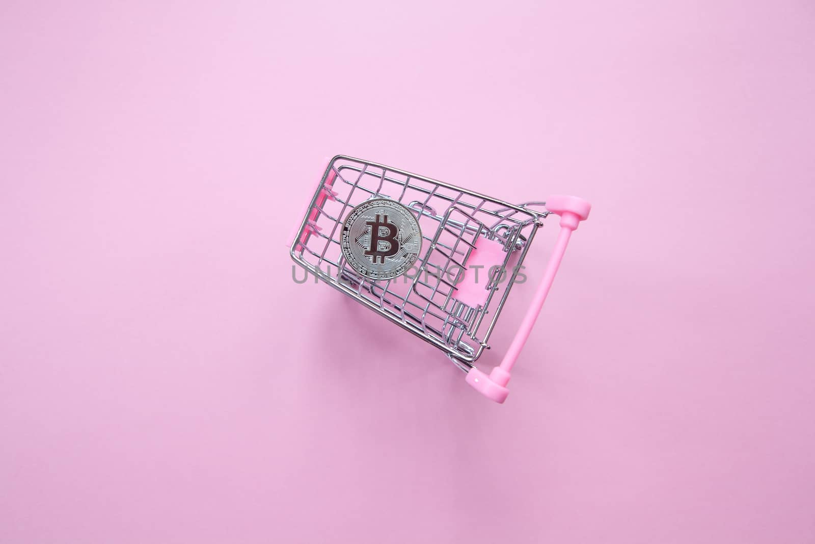 Silver bitcoin in shopping truck on a millennial pink background. Top view. Minimalism. Horizontal orientation.