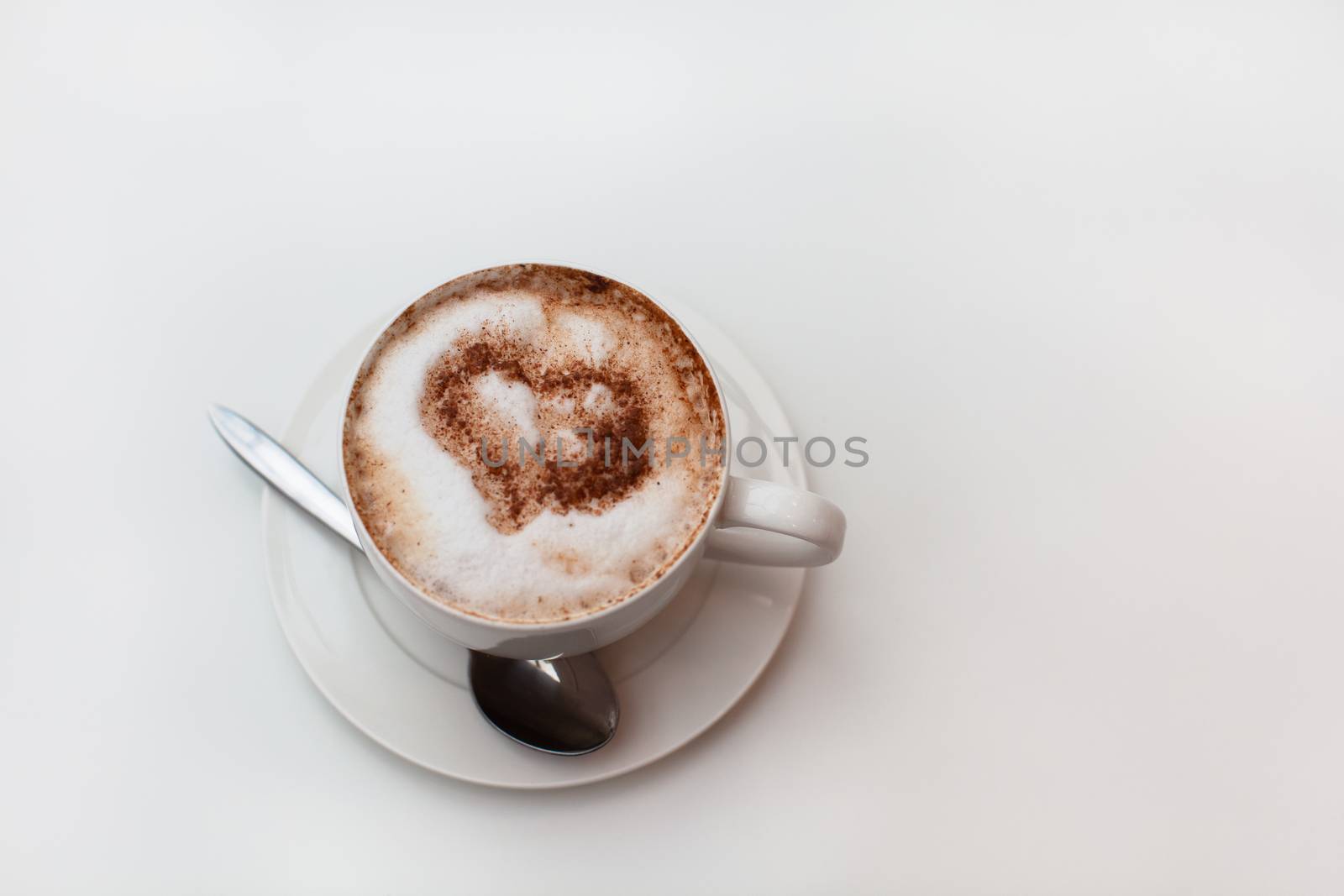 Cappuccino cup on white table background. Foam is decorated with cinnamon heart. Copy space. Top view, located at side of frame. Horizontal. Lactose free concept. Soft focus