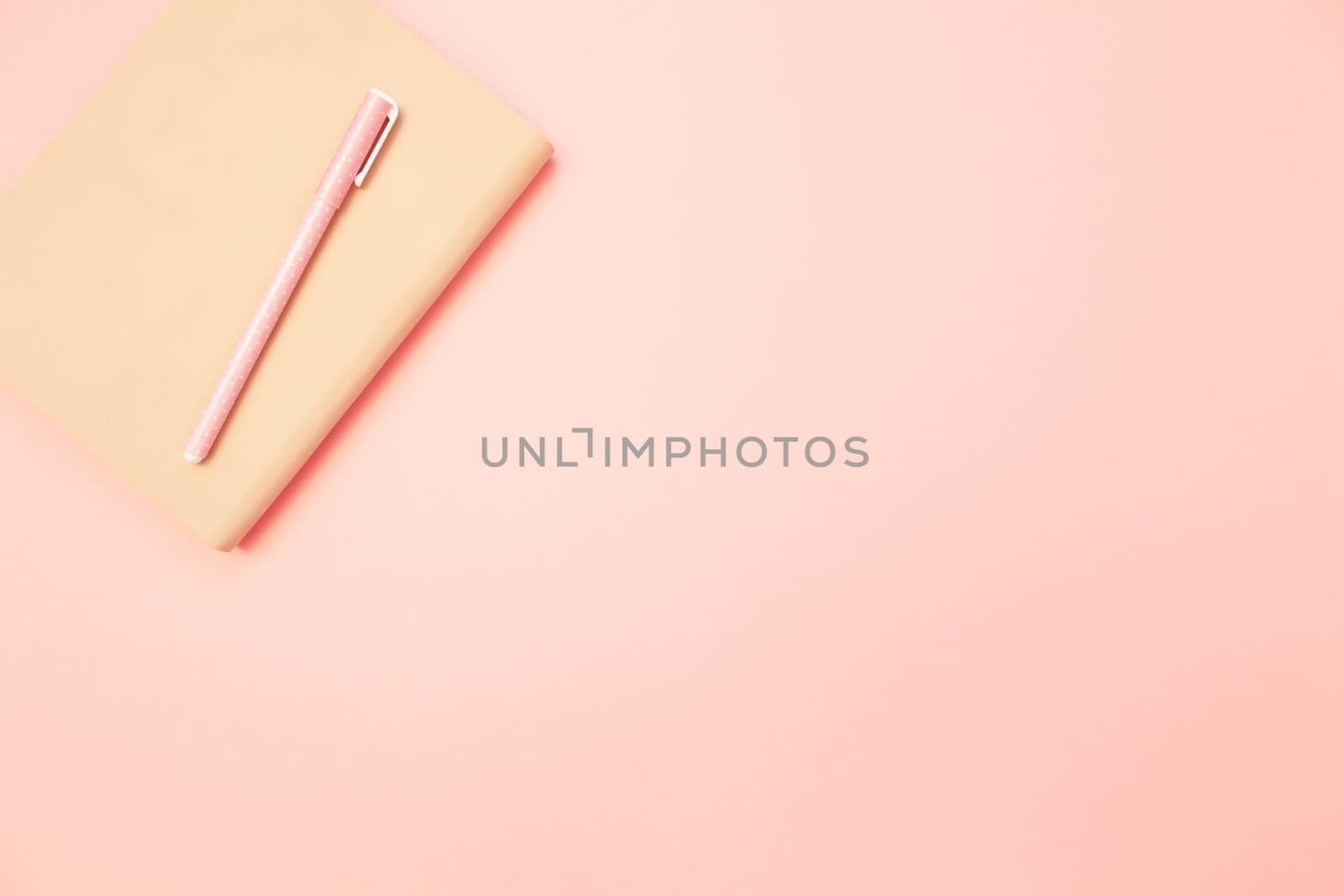 Beige diary with pink pen on pastel millennial pink paper background. Concept of education, blogging. Top view. Flat lay. Minimal style. Template for female blog. Lifestyle. Copy space.