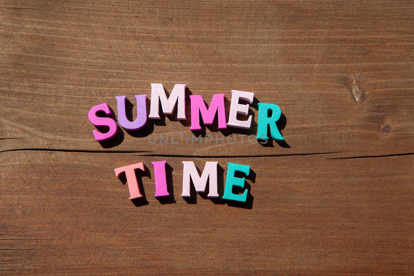 Inscription summertime by multicoloured wooden letters on wooden surface. Concept happy summertime.