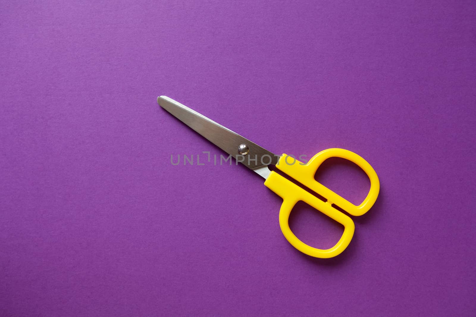 Yellow kid's stationery right-handed scissors on purple papper background. Back to school, DIY concept. Top view, copy space