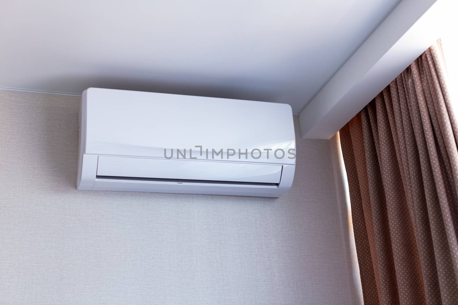 Small air conditioning on the wall inside room in apartment, switched off. Interior in calm beige tones.