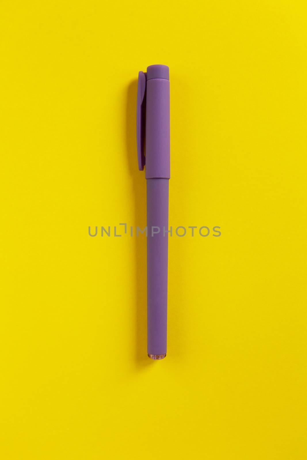 Purple pen on yellow paper background. Central composition. Contrast colours. Back to school, education concept. Top view. Flat lay. Vertical. Minimal style.