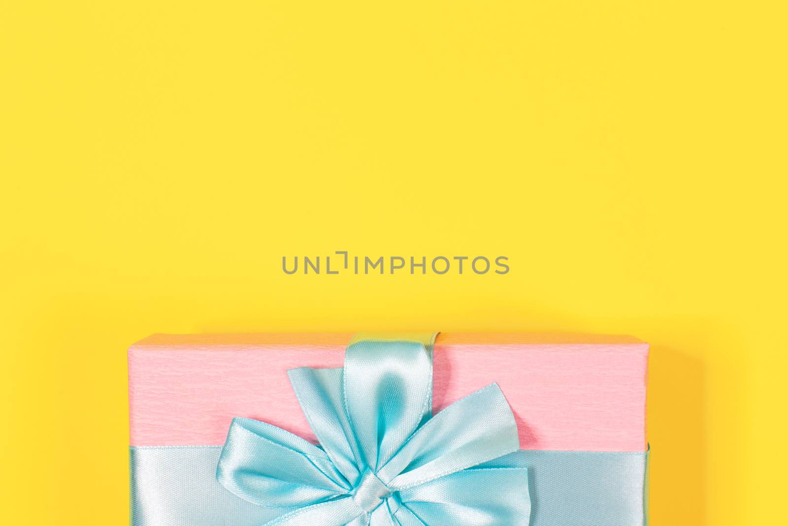 Pink gift box tied with blue ribbon with bow at the top on yellow background. Copy space for text. Minimal flat lay. Top view. Birthday, New year, Mother's day, Women's day celebration concept