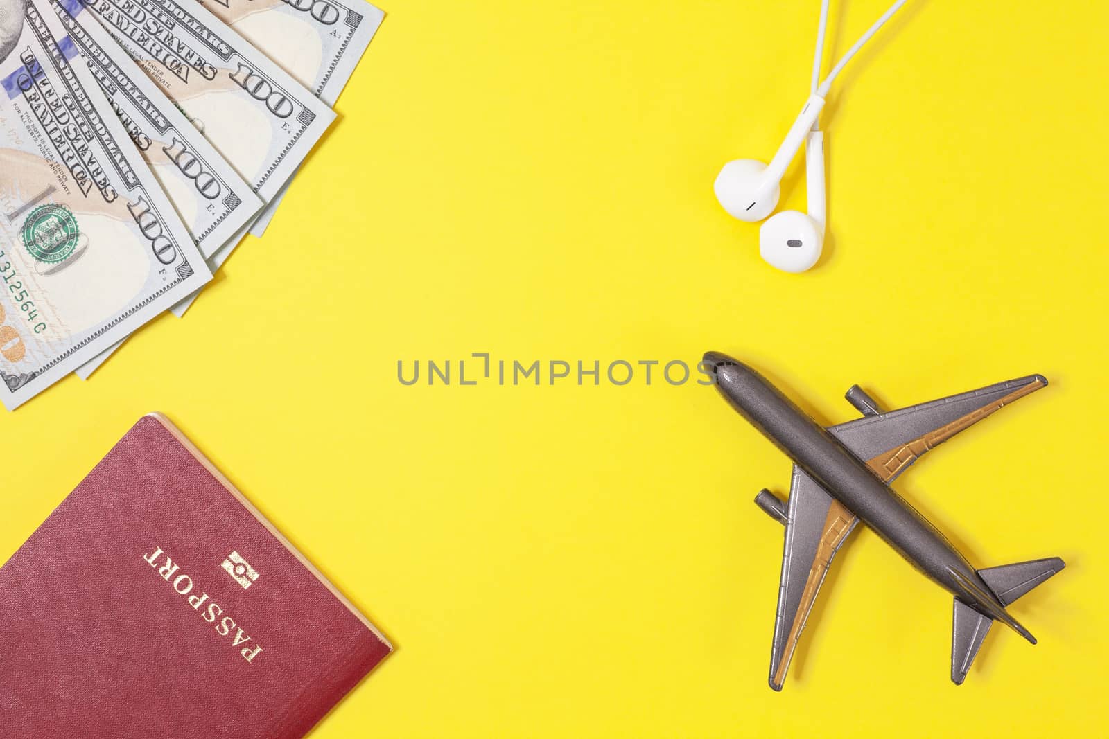 One hundred dollar bills, airplane, headphones, foreign passport on bright yellow paper background. Copy space. Travel and business concept, flat lay. Hand luggage, minimalism, frame of objects