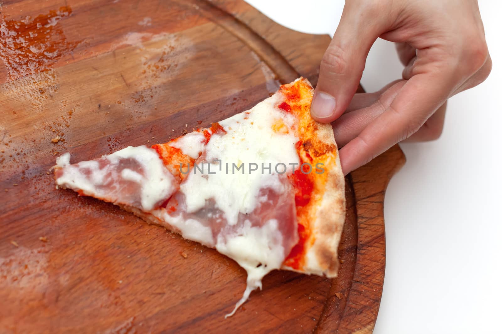 Man took last one slice of delicious Italian pizza. In frame hand taking slice of hot pizza with ham on wooden board on white table. Pizza time. Side view. Close-up