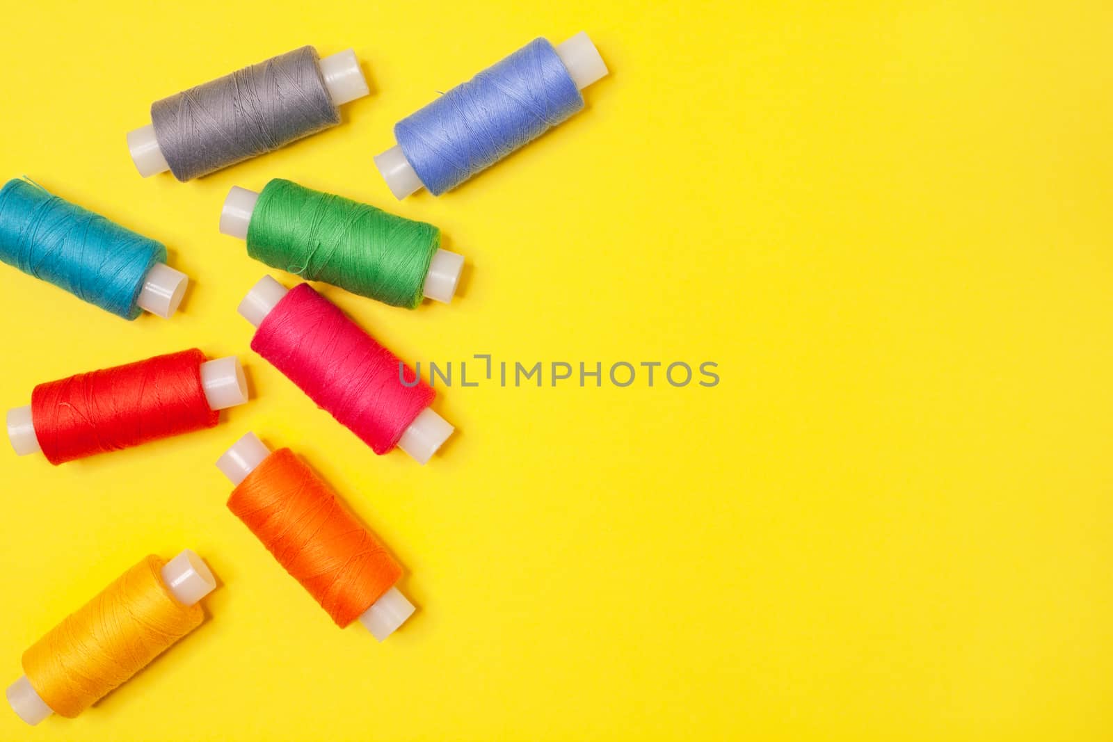 Handicraft background. Set of multicolored spools of thread on yellow background with copy space. Accessories for needlework, embroidery, sewing. Flat lay. Top view. Items scattered on left side.
