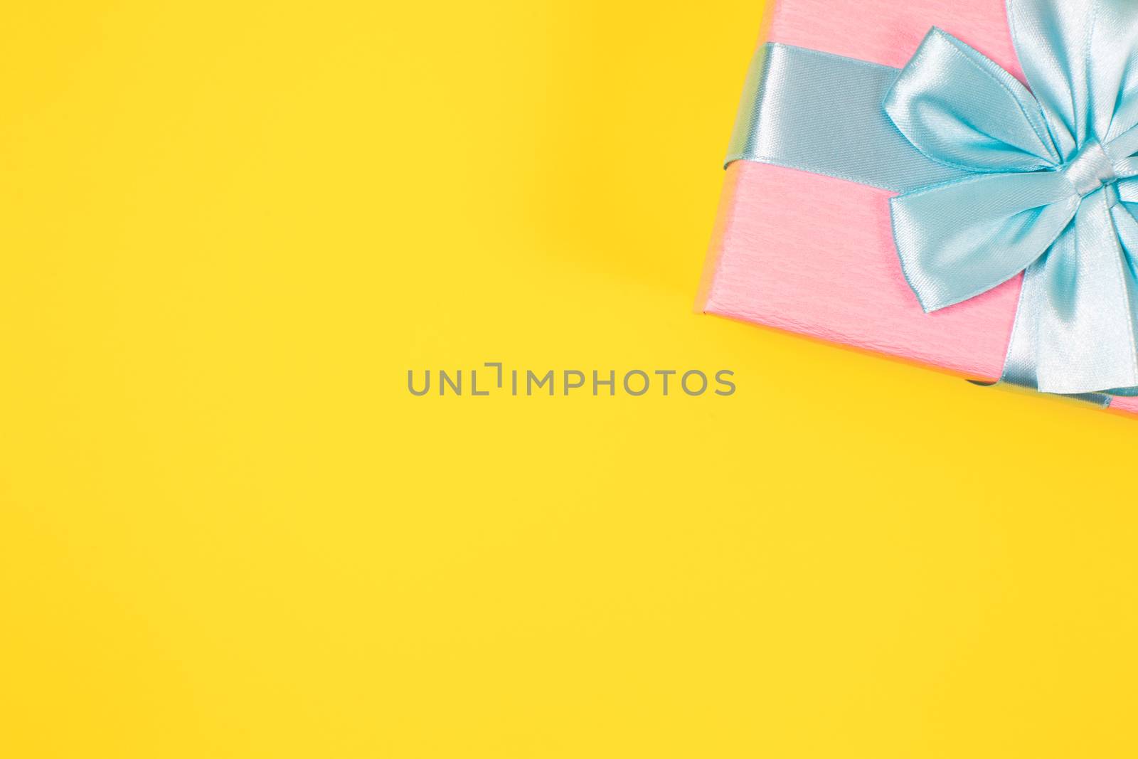 Pink gift box tied with blue ribbon with bow at the top on yellow background. Copy space for text. Minimal flat lay. Top view. Birthday, New year, Mother's day, Women's day celebration concept