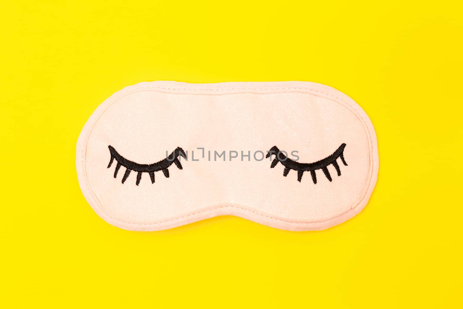 Pastel pink sleep mask with closed eyes embroidered on it with eyelashes on bright yellow neon background. Fashion accessory for sleep. Concept of vivid dreams, accessories for girls and young women