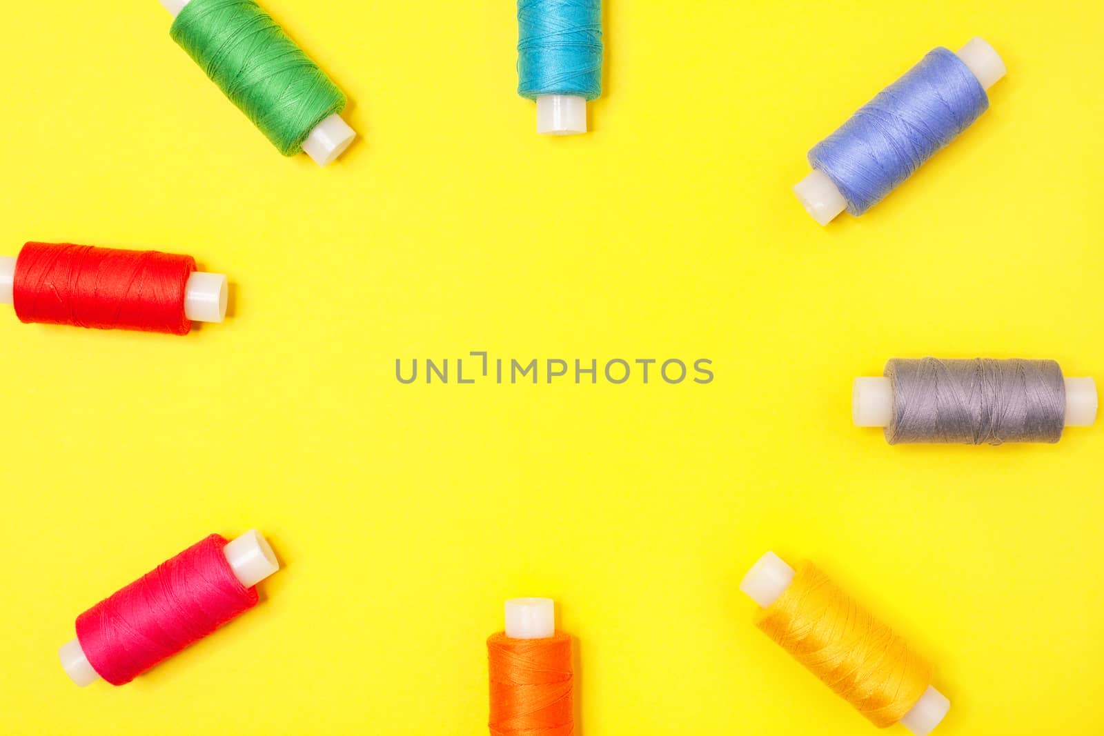 Handicraft background. Set of multicolored spools of thread form frame on yellow background with copy space. Accessories for needlework, embroidery, sewing. Flat lay. Top view