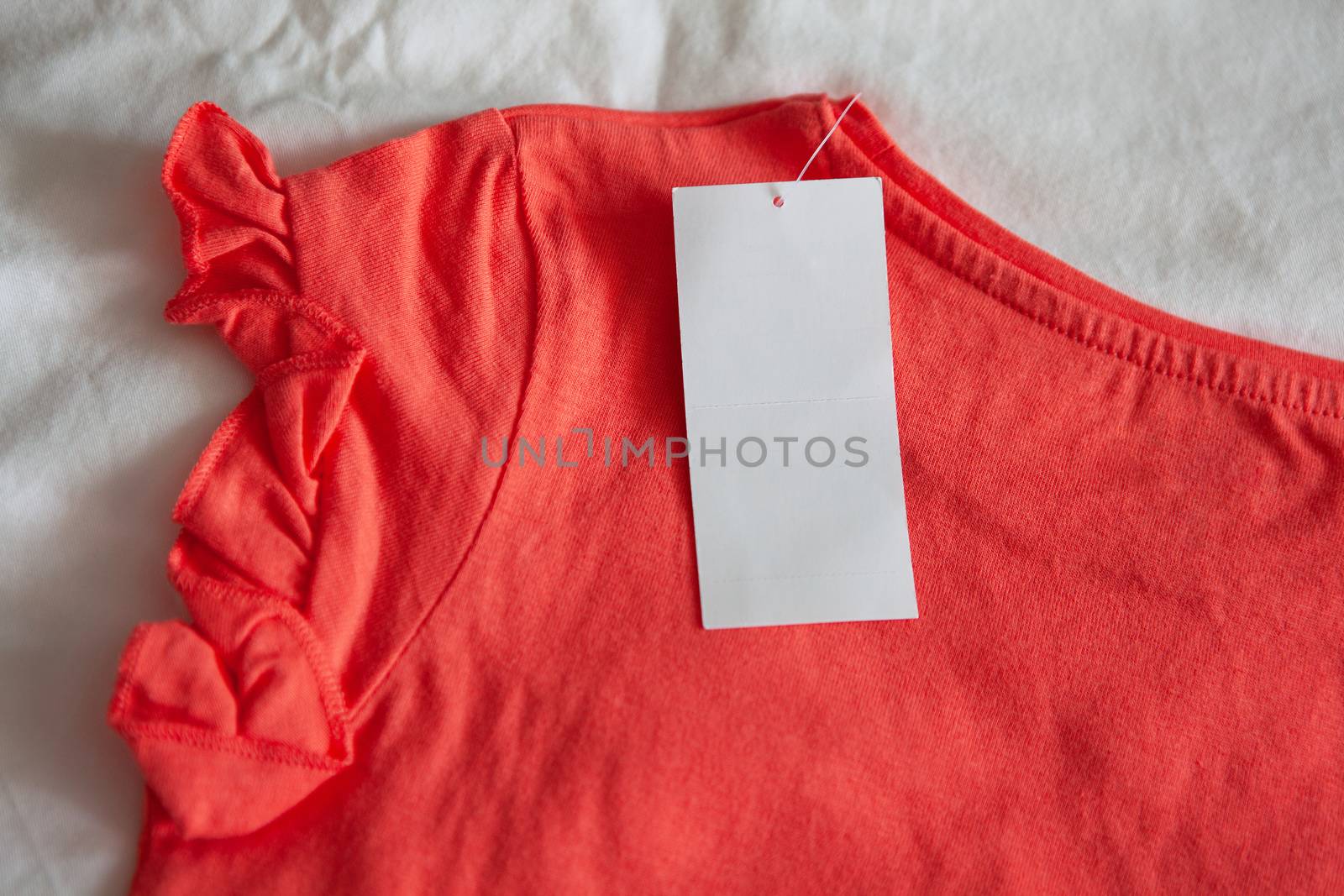 New pink red kid's or women's t-shirt with tag on white background. Concept shopping, summer sales, discounts, organic cotton clothes, recycled clothing