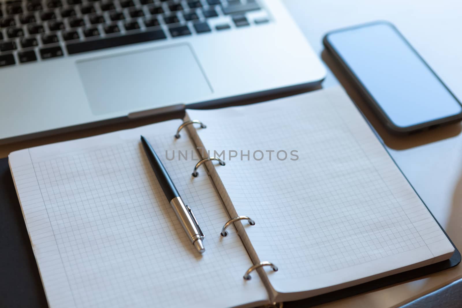 Working space, top view. Laptop, mobile phone and open notebook with pen on beige desktop. Notepad sheets on silver brackets, automatic ballpoint pen in silver-black colour. Business background