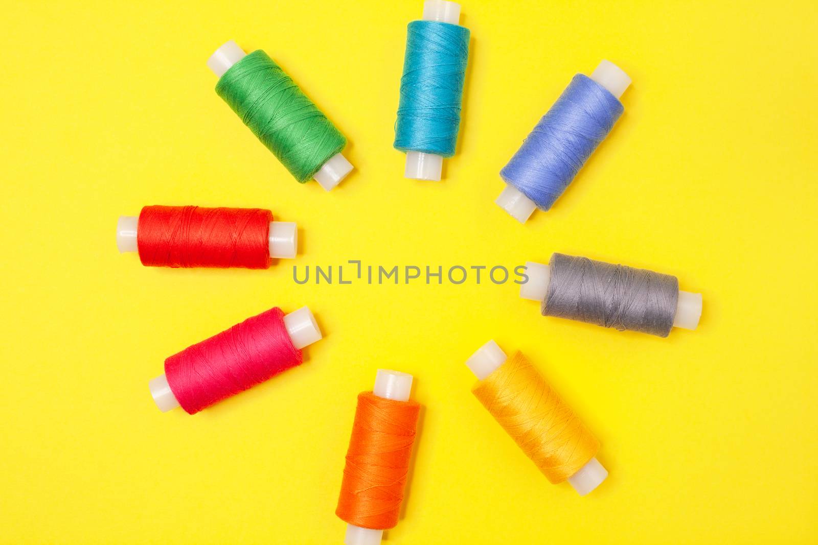 Set of multicolored spools of thread on yellow background. Accessories for needlework, embroidery, sewing. Flat lay. Top view. Objects are located in center, forming flower.