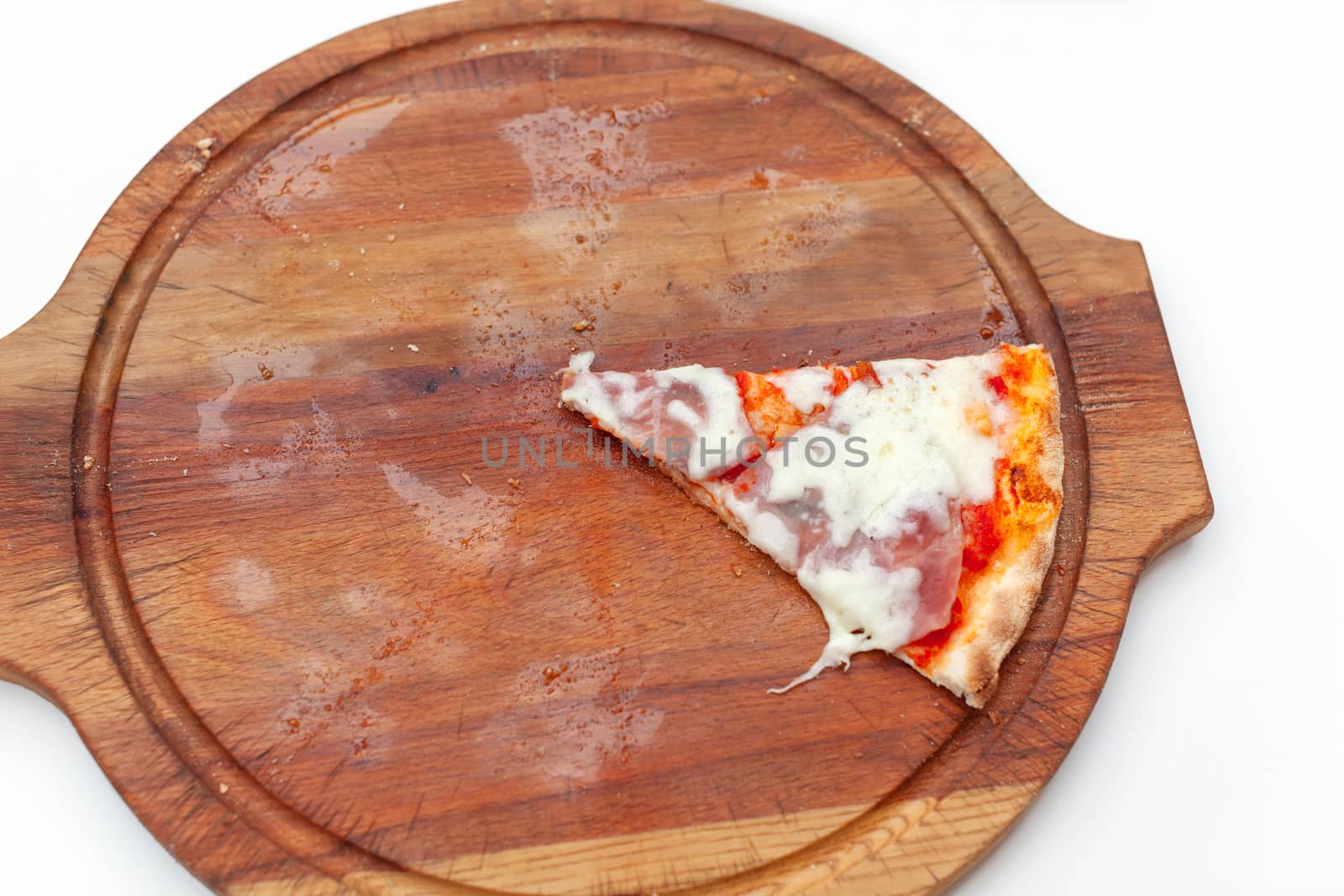 Last one slice of delicious Italian pizza with ham and cheese on wooden board on white table. Pizza time. Top view. Close-up