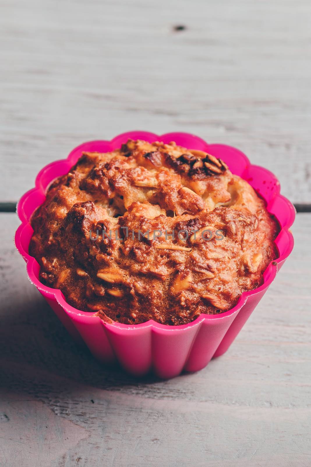 Cooked oatmeal muffin in a pink silicone bakeware over light wooden background.