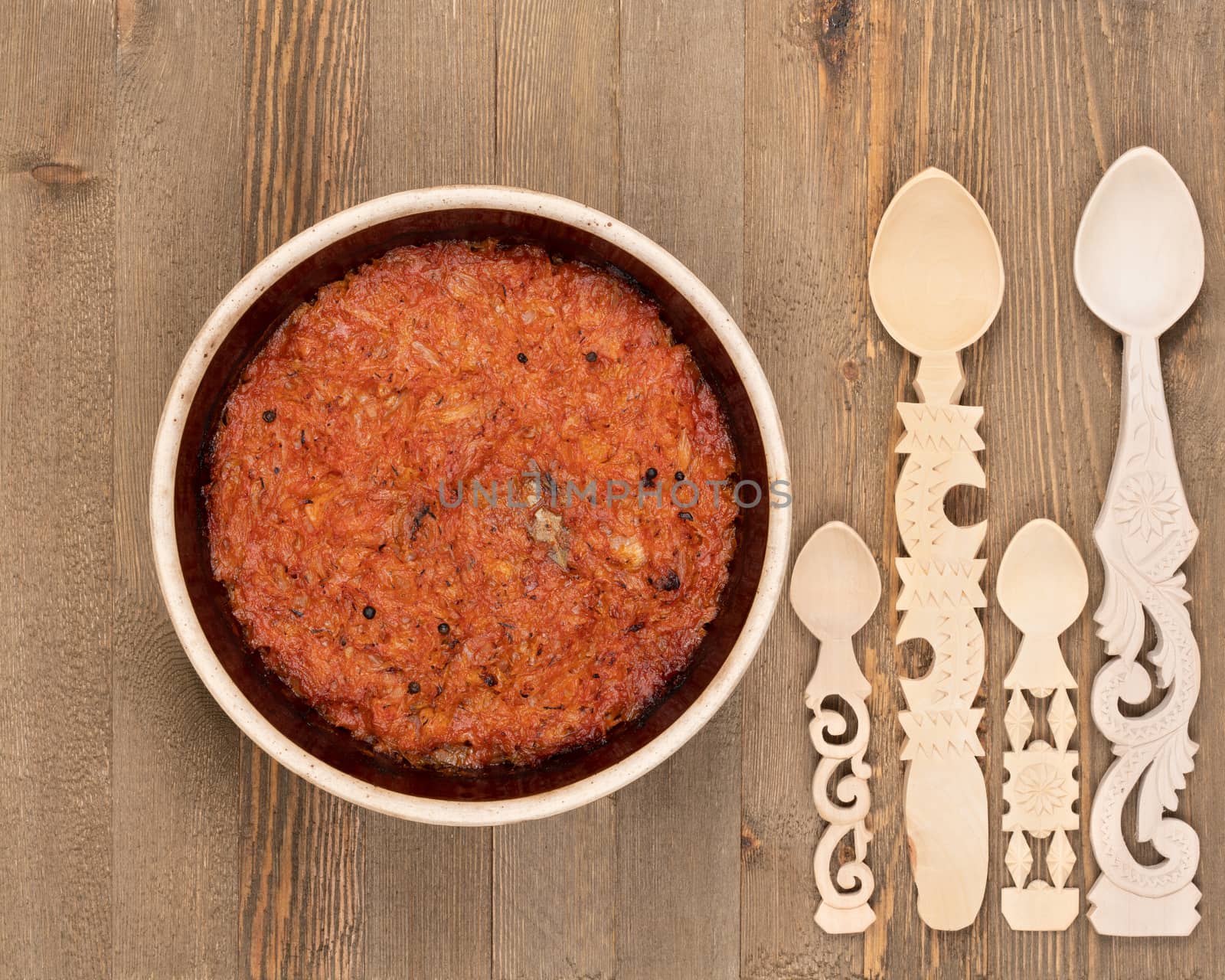 A ceramic pot of traditional Eastern European stewed cabbage and decorated wooden spoons on a brown wooden kitchen board.