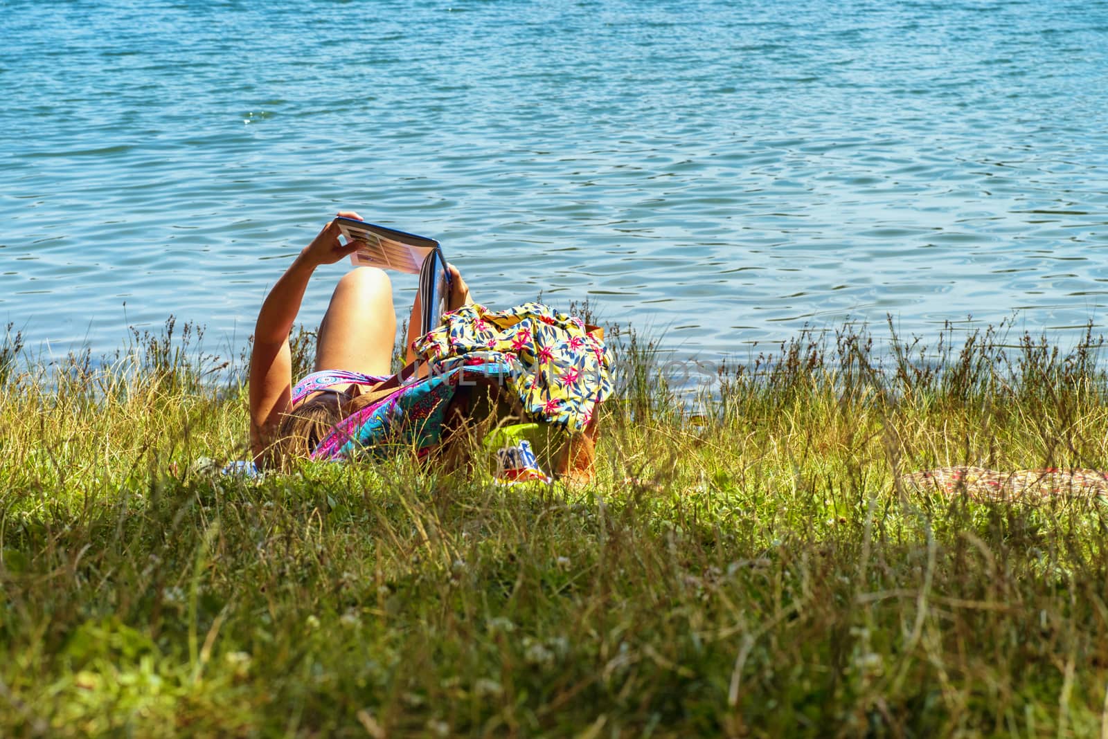 A girl lies in a river and reads a book. Young woman reading a book sitting by the river.