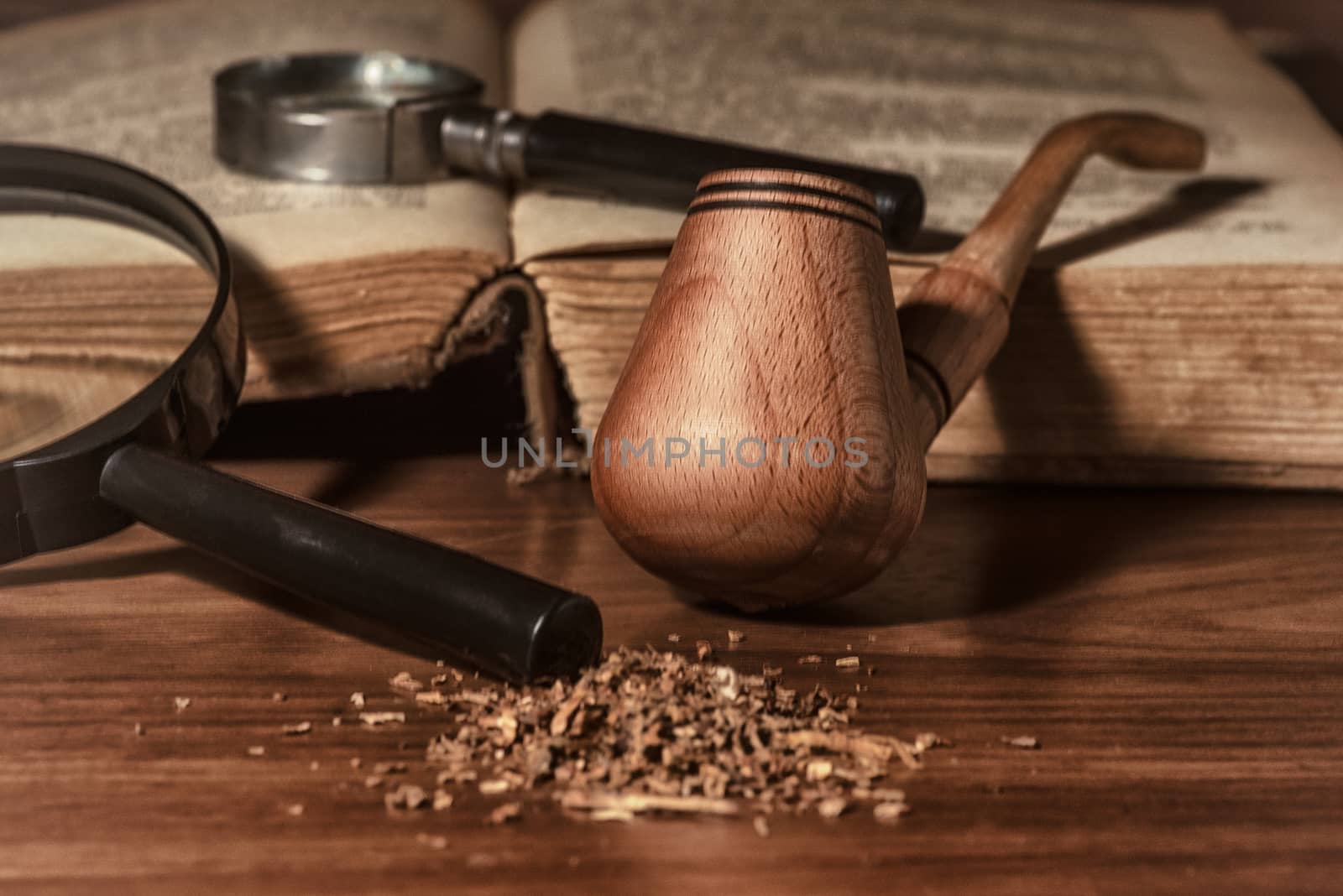 Wooden pipe with smoke on heap of chopped dried tobacco leaves against black background.