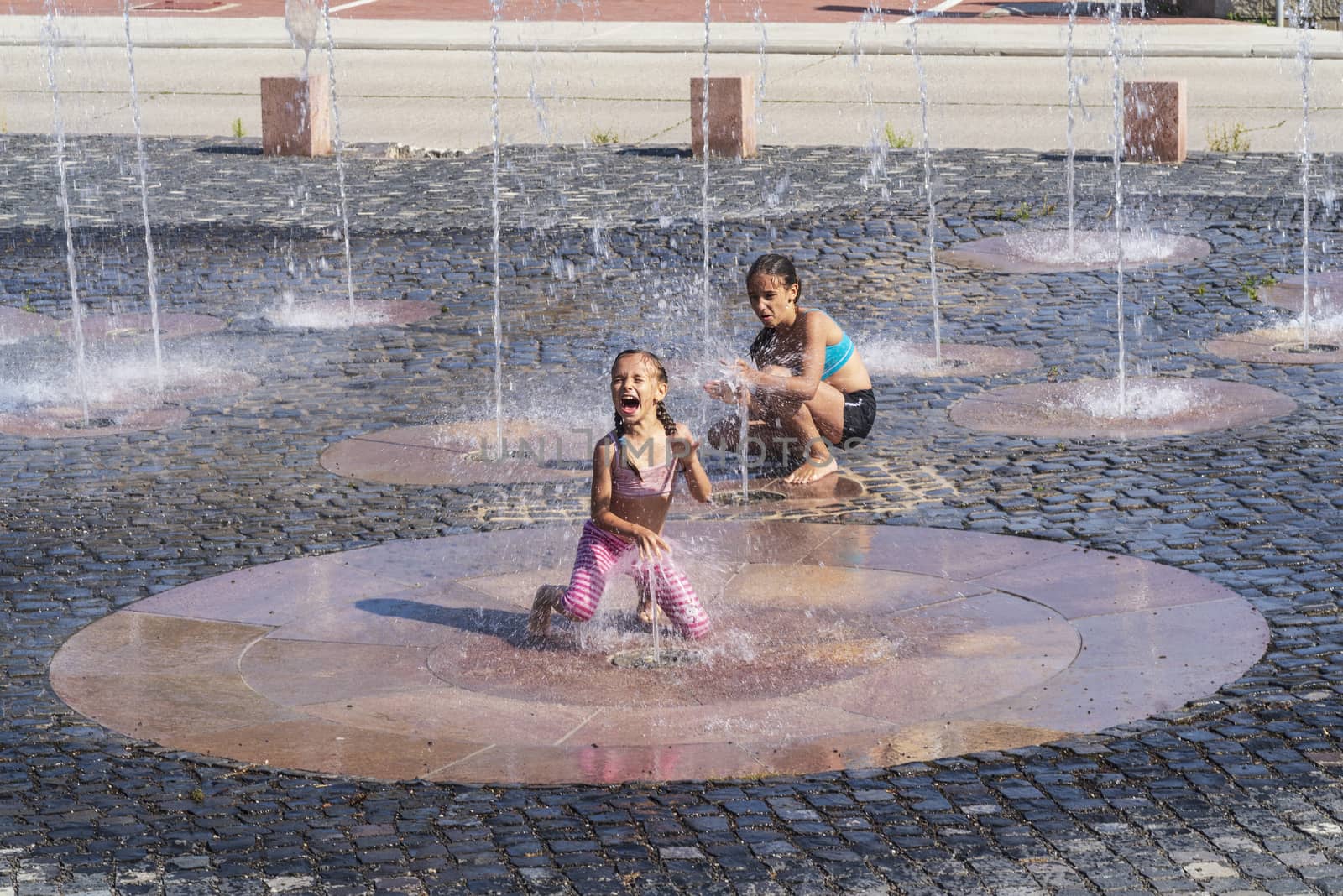 Children on a sunny summer day are poured water from a fountain.Children happily in shallow clean water on of city fountain on warm bright summer day.