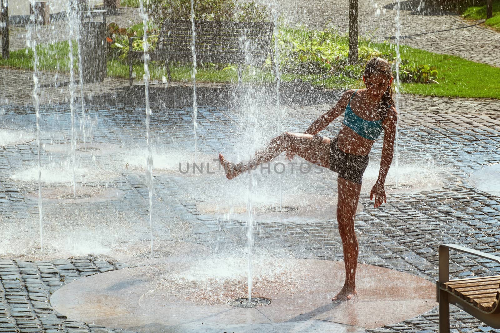 Girl on a sunny summer day are poured water from a fountain.Girl happily in shallow clean water on of city fountain on warm bright summer day.