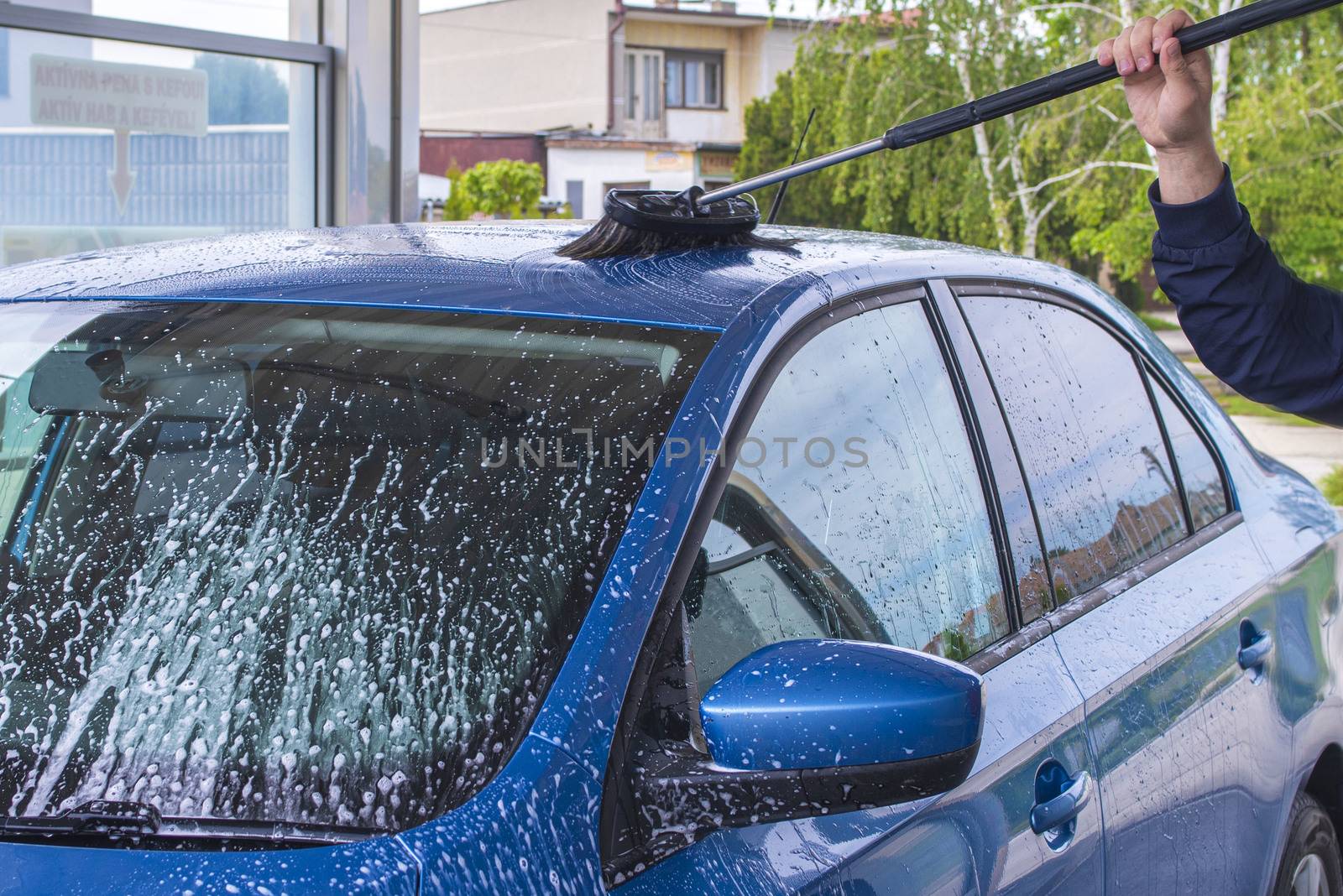 Manual car wash with pressurized water in car wash outside.Using a brush to wash a car on a car washing facility on sunny summer day.Blue car manual wash of with pressurized water in car wash outside.