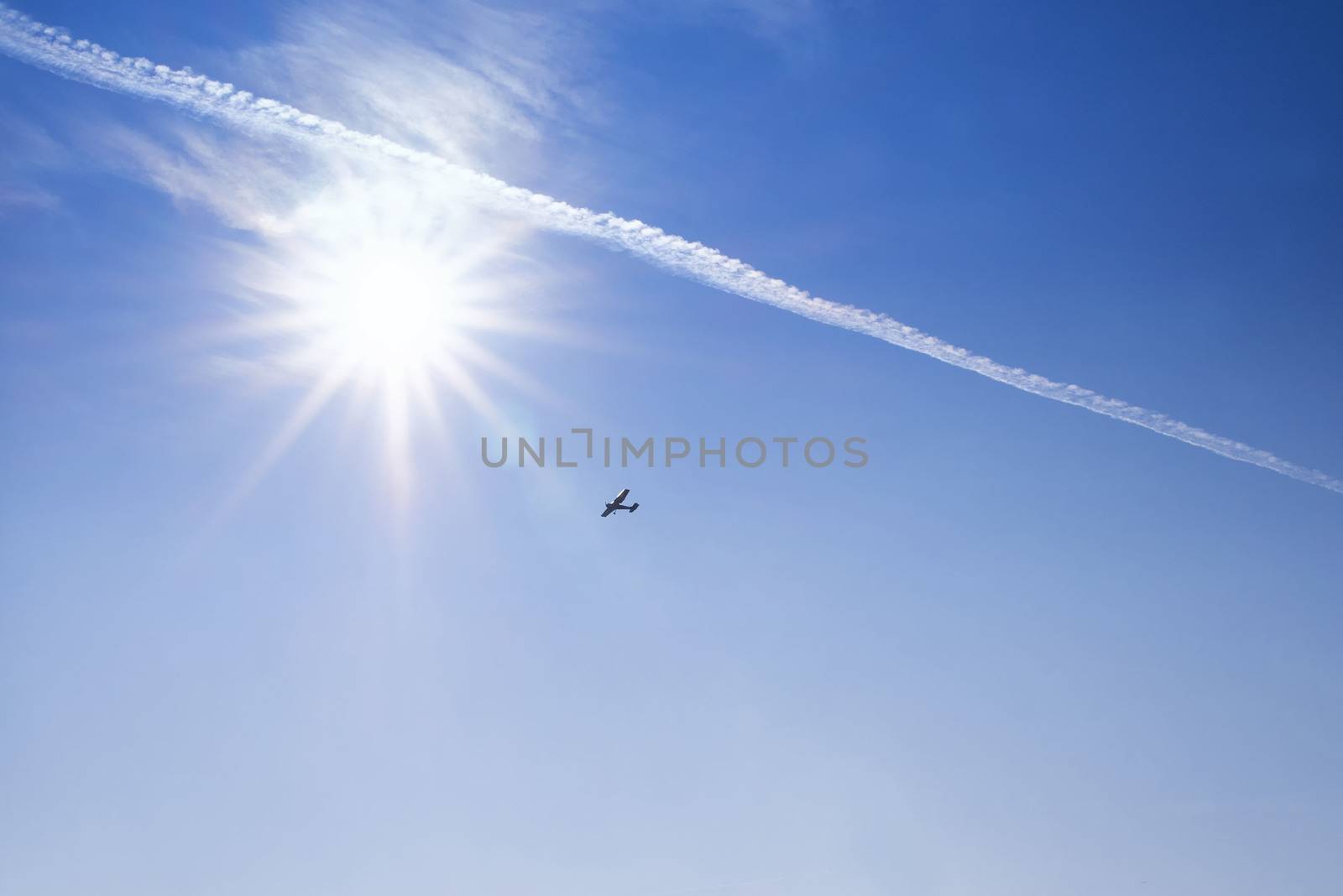Blue sky . Against the background of blue sky and bright sun, an airplane is flying. Basic background for design.Aircraft flying in the sky against a background of a bright sunset.