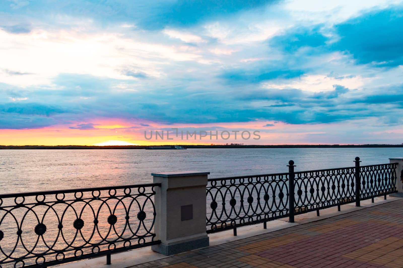 Sunset on the embankment of the Amur river in Khabarovsk. The sun set over the horizon. The embankment is lit by lanterns.