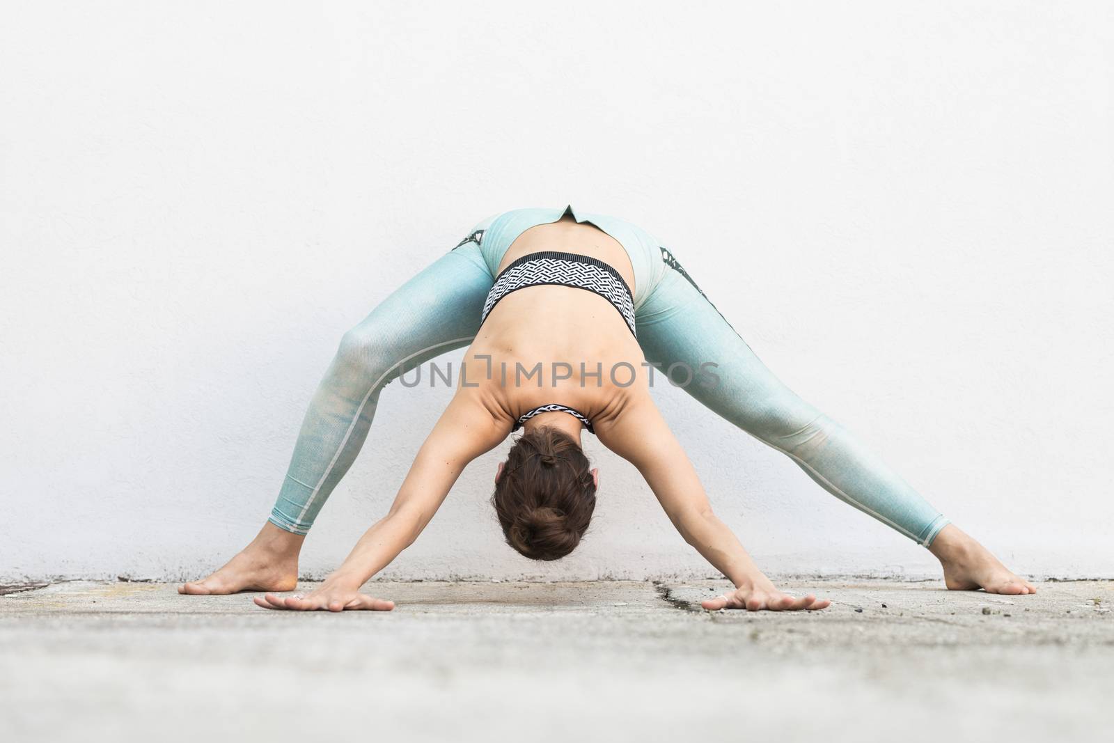 Fit sporty active girl in fashion sportswear doing yoga fitness exercise in front of gray wall, outdoor sports, urban style.