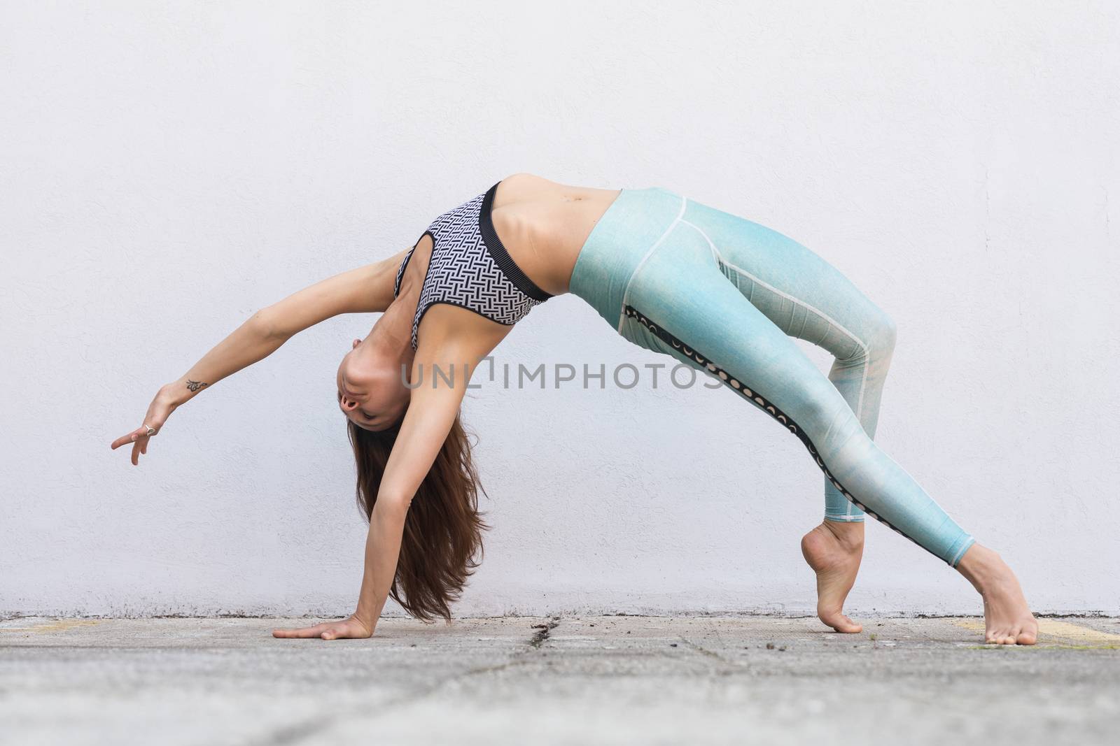 Fit sporty active girl in fashion sportswear doing yoga fitness exercise in front of gray wall, outdoor sports, urban style.