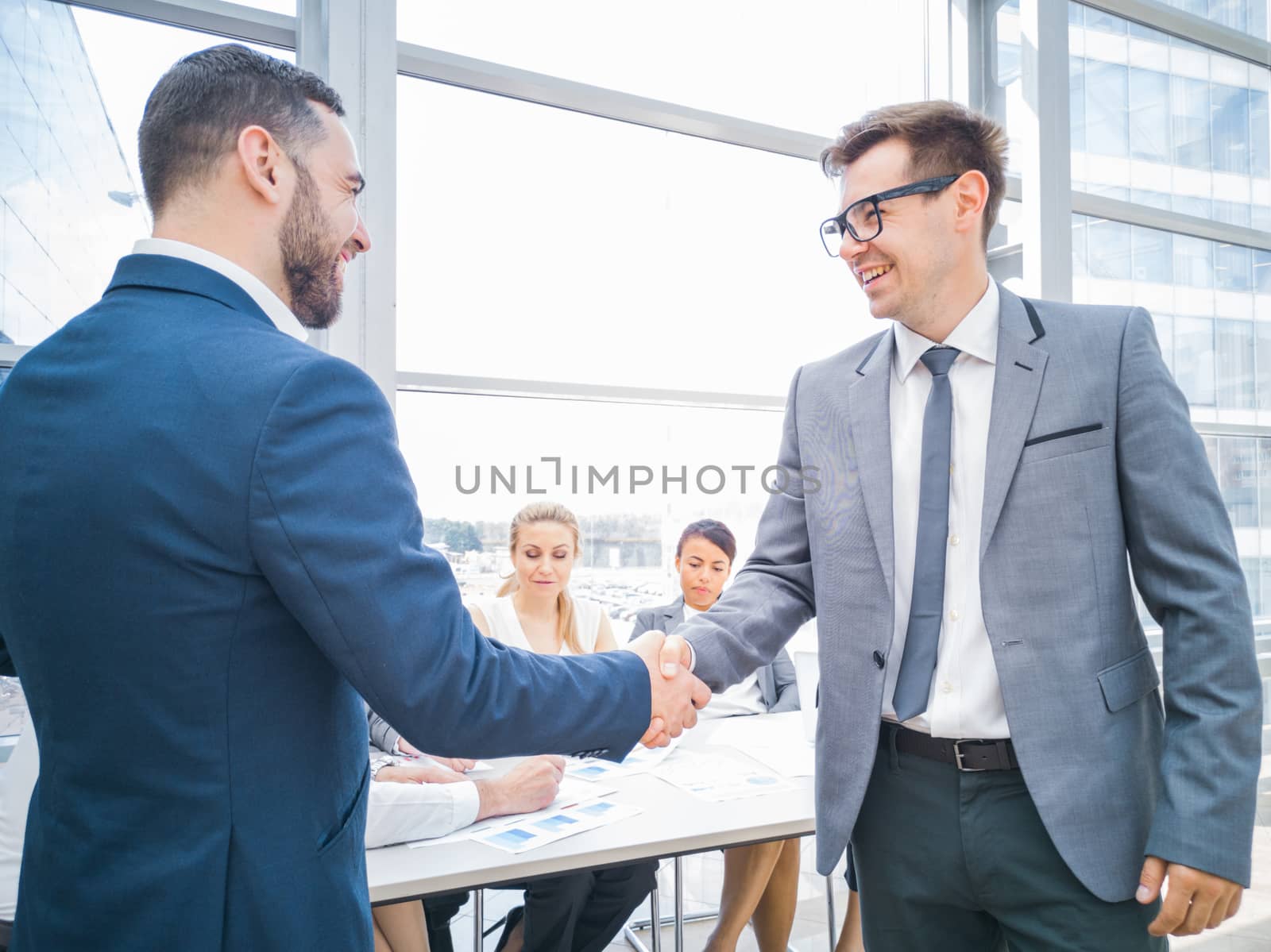 Handshake of business partners after discussion of the financial reports, their team on background