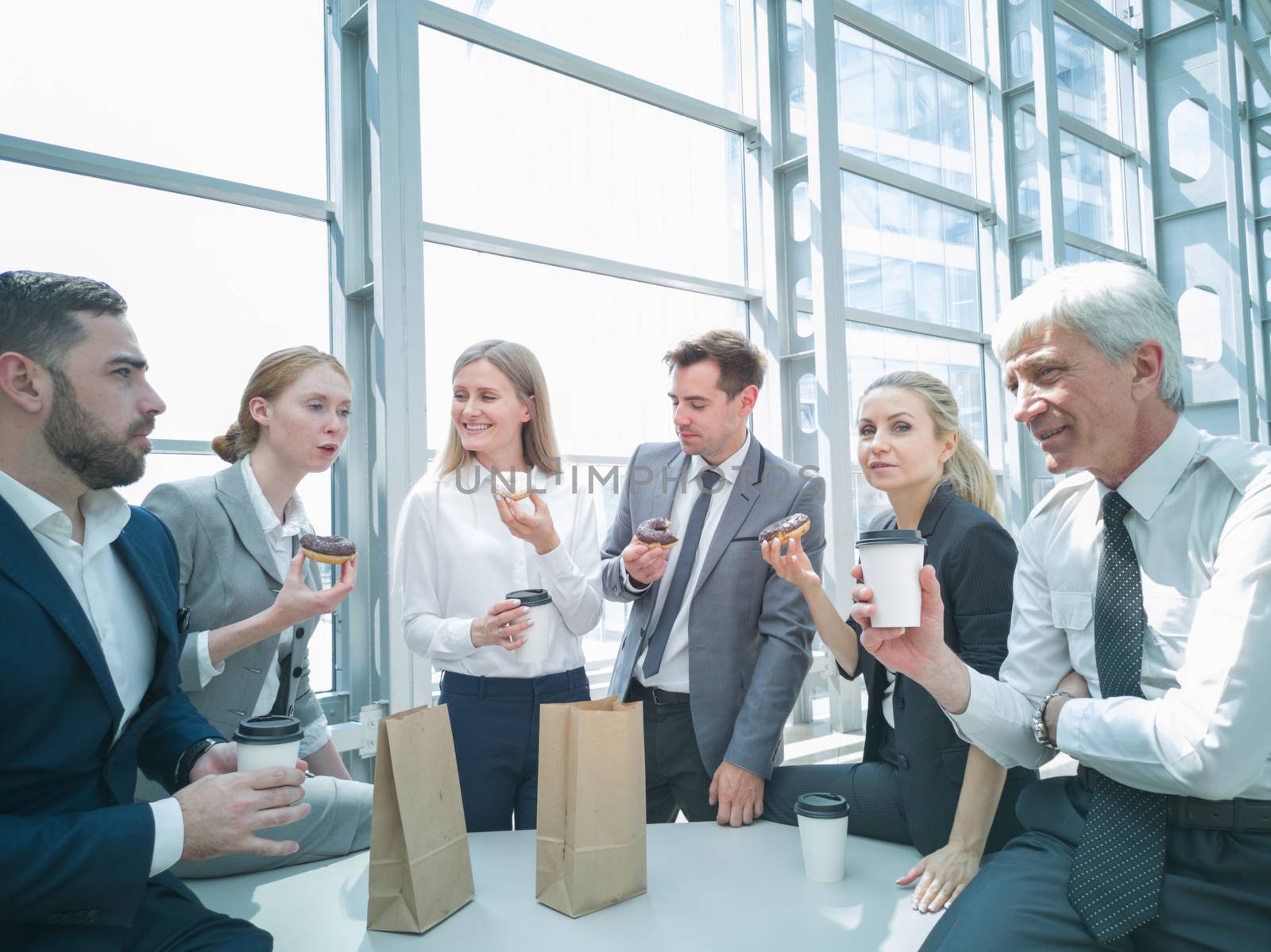 Business people having coffee break eating donuts together in office