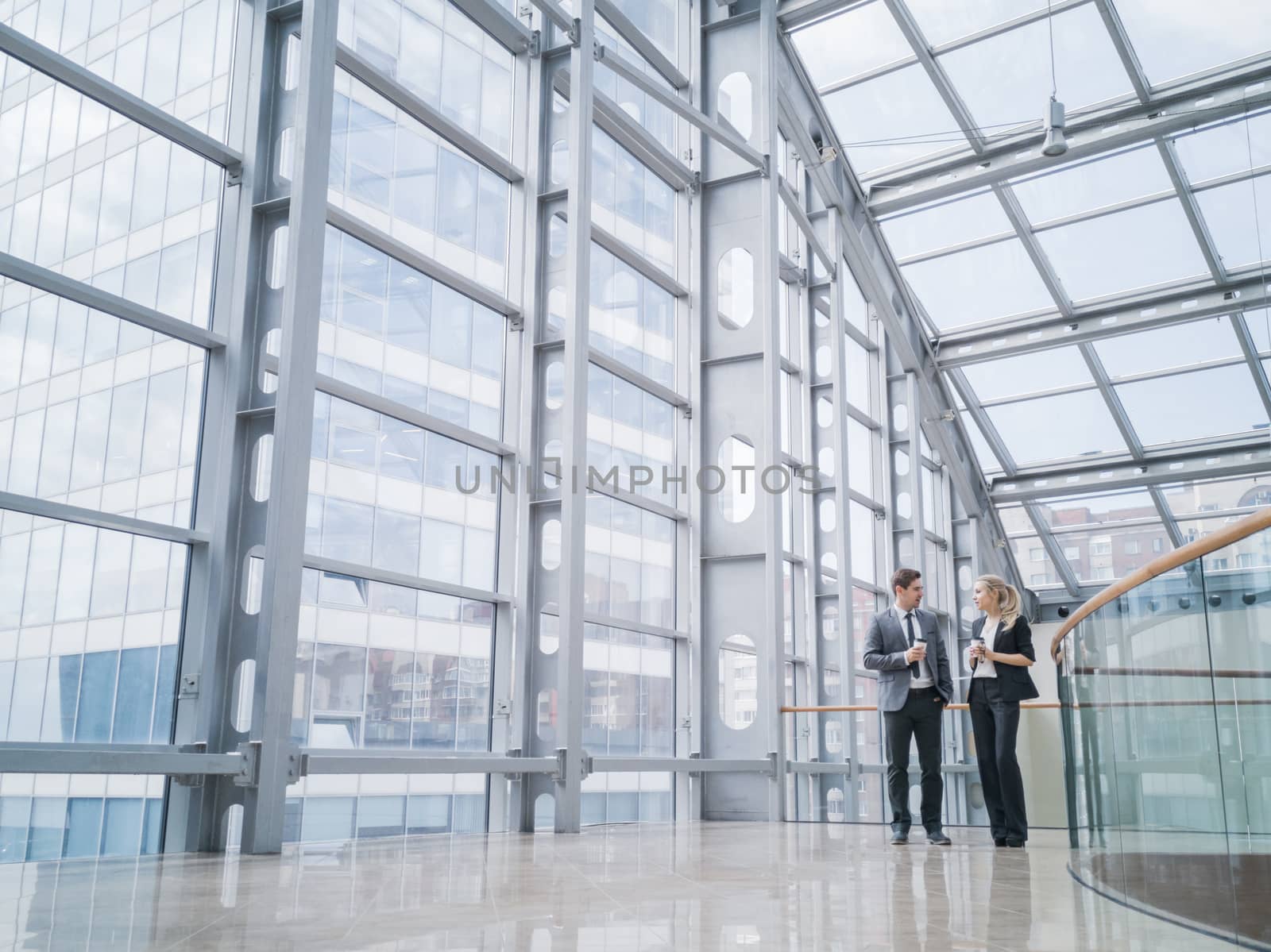 Businessman and businesswoman walk together and talk about business holding coffee in hand