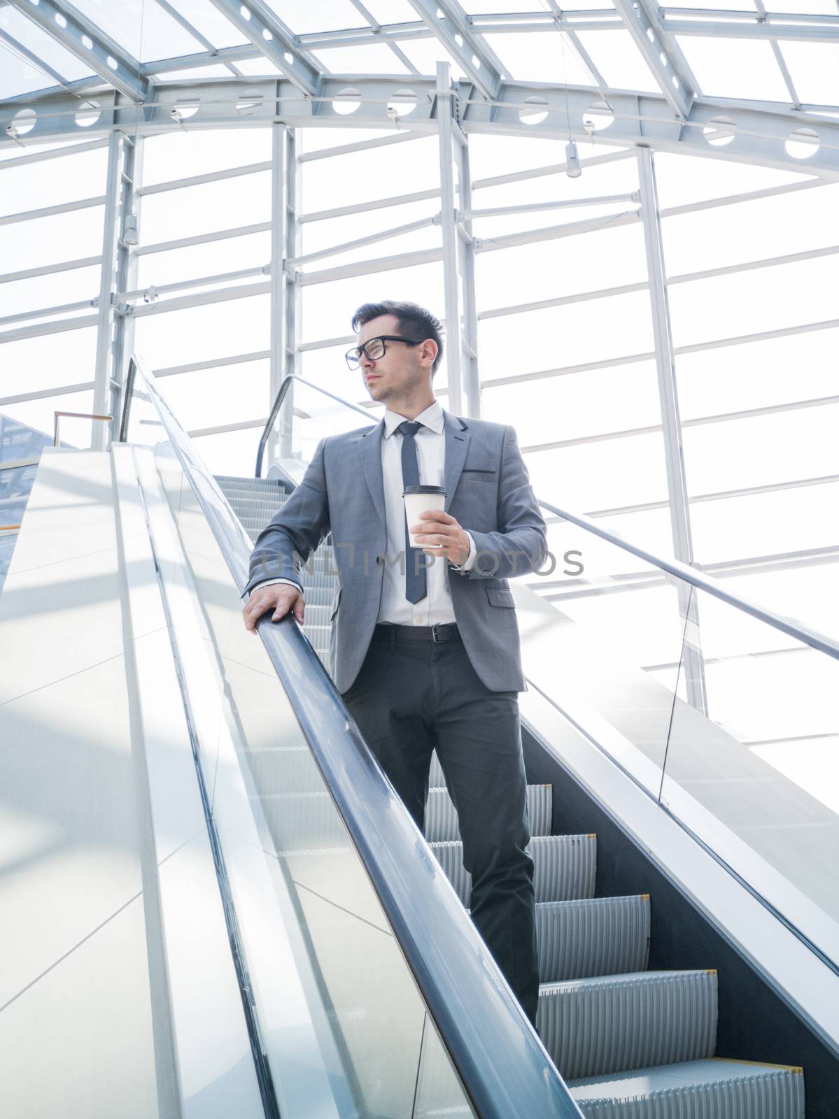 Businessman on escalator holding coffee in hand