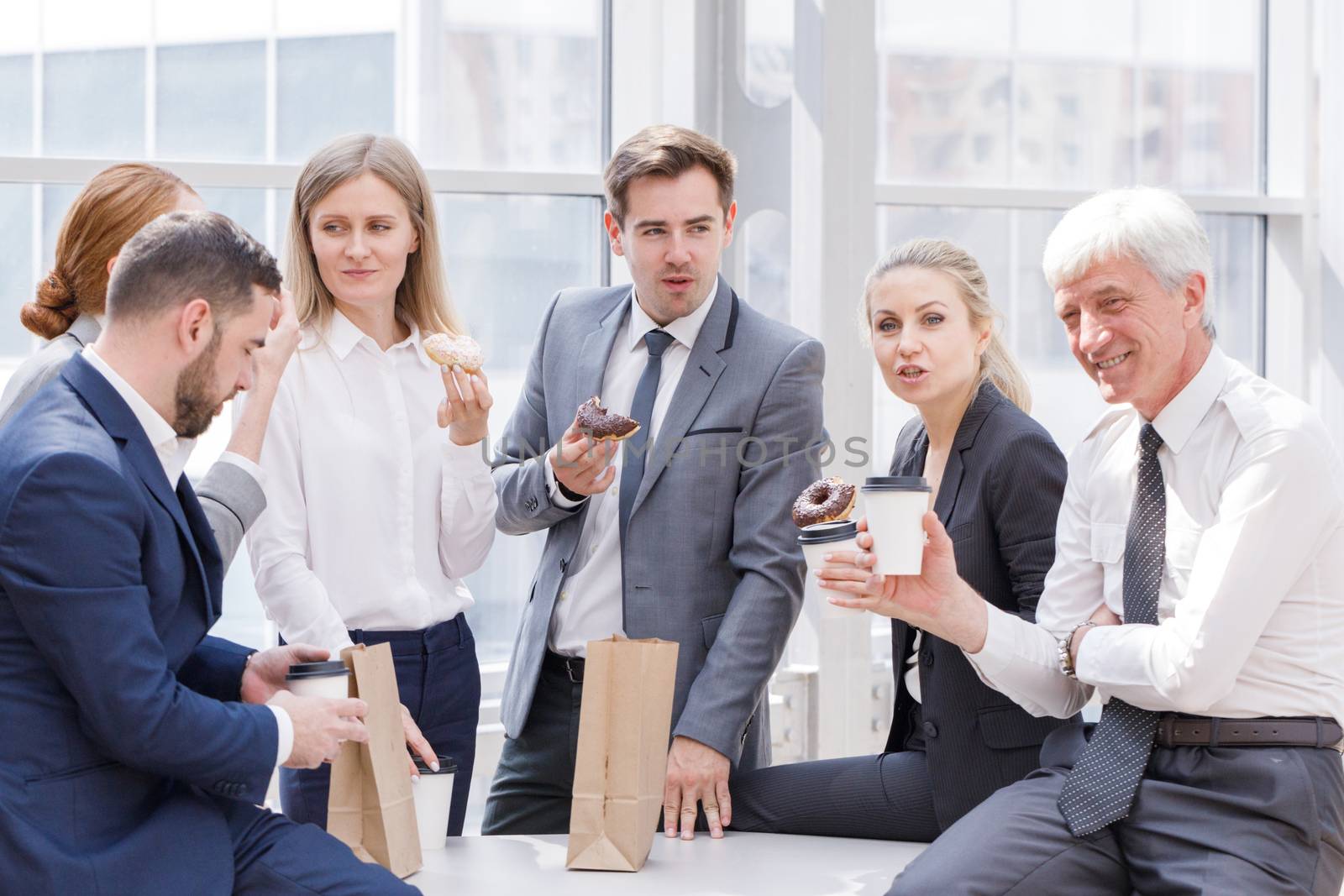 Business people having coffee break eating donuts together in office