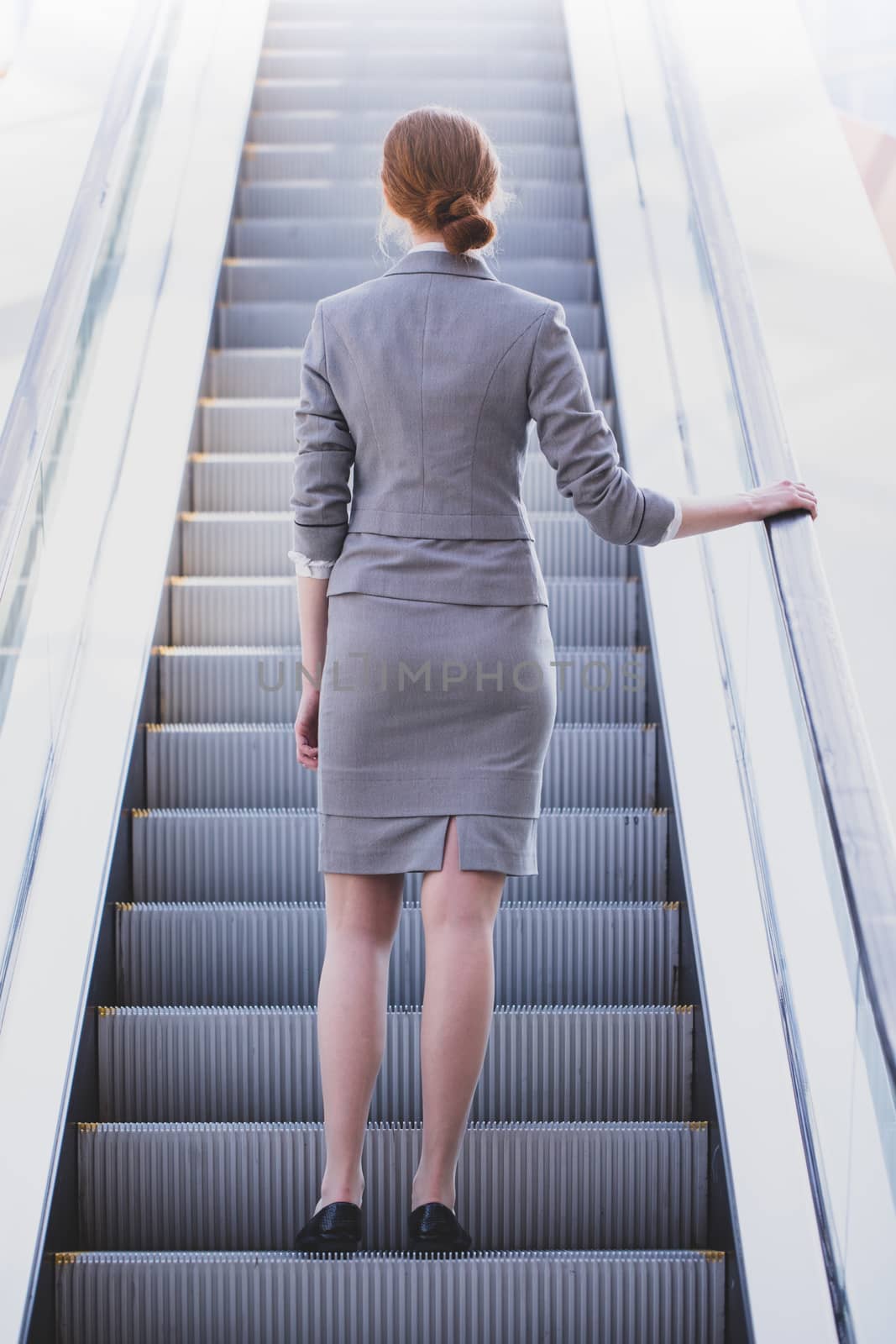 Back view of attractive business woman in suit on escalator