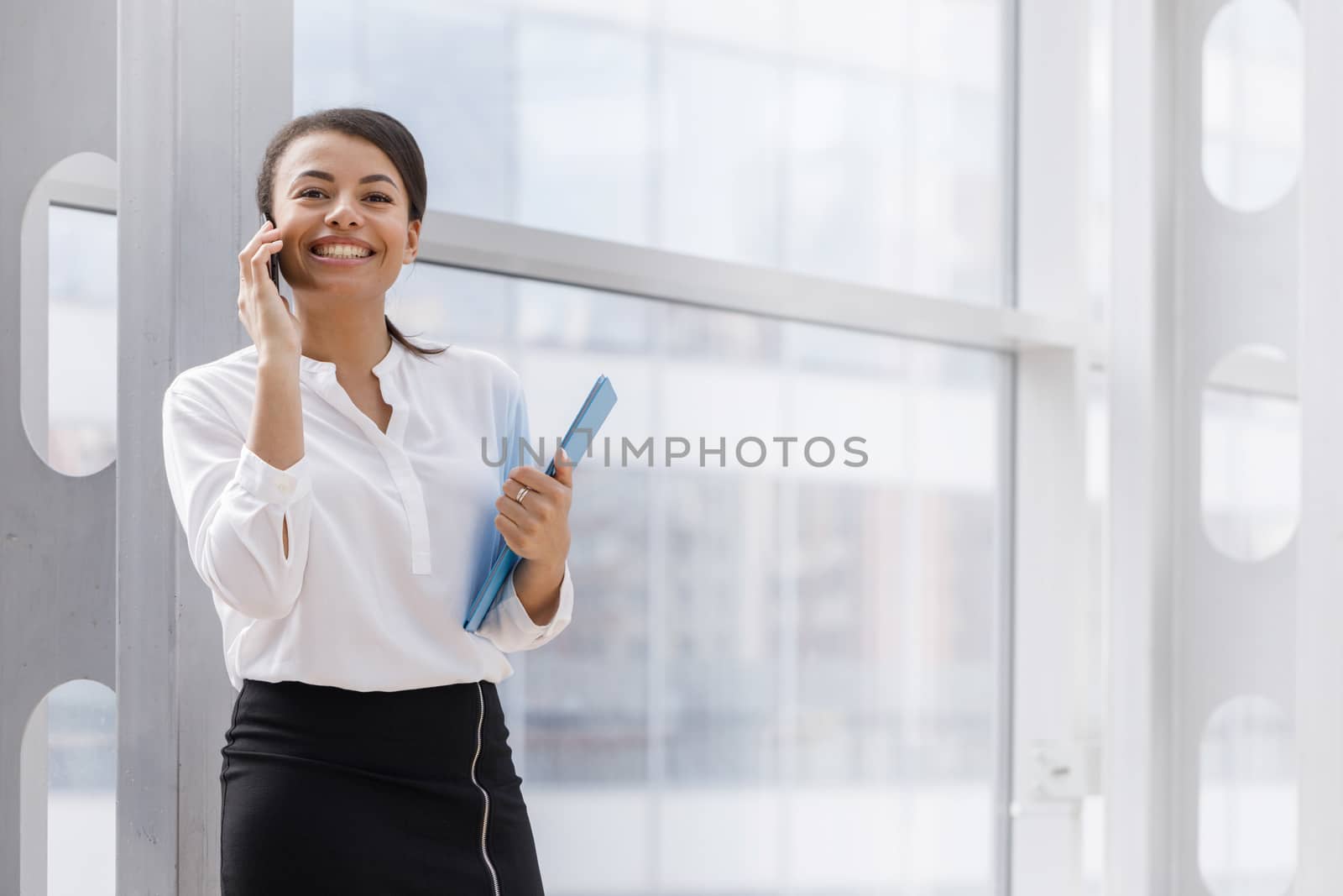 Happy african businesswoman smiling and talking on the phone, holding folder of documents