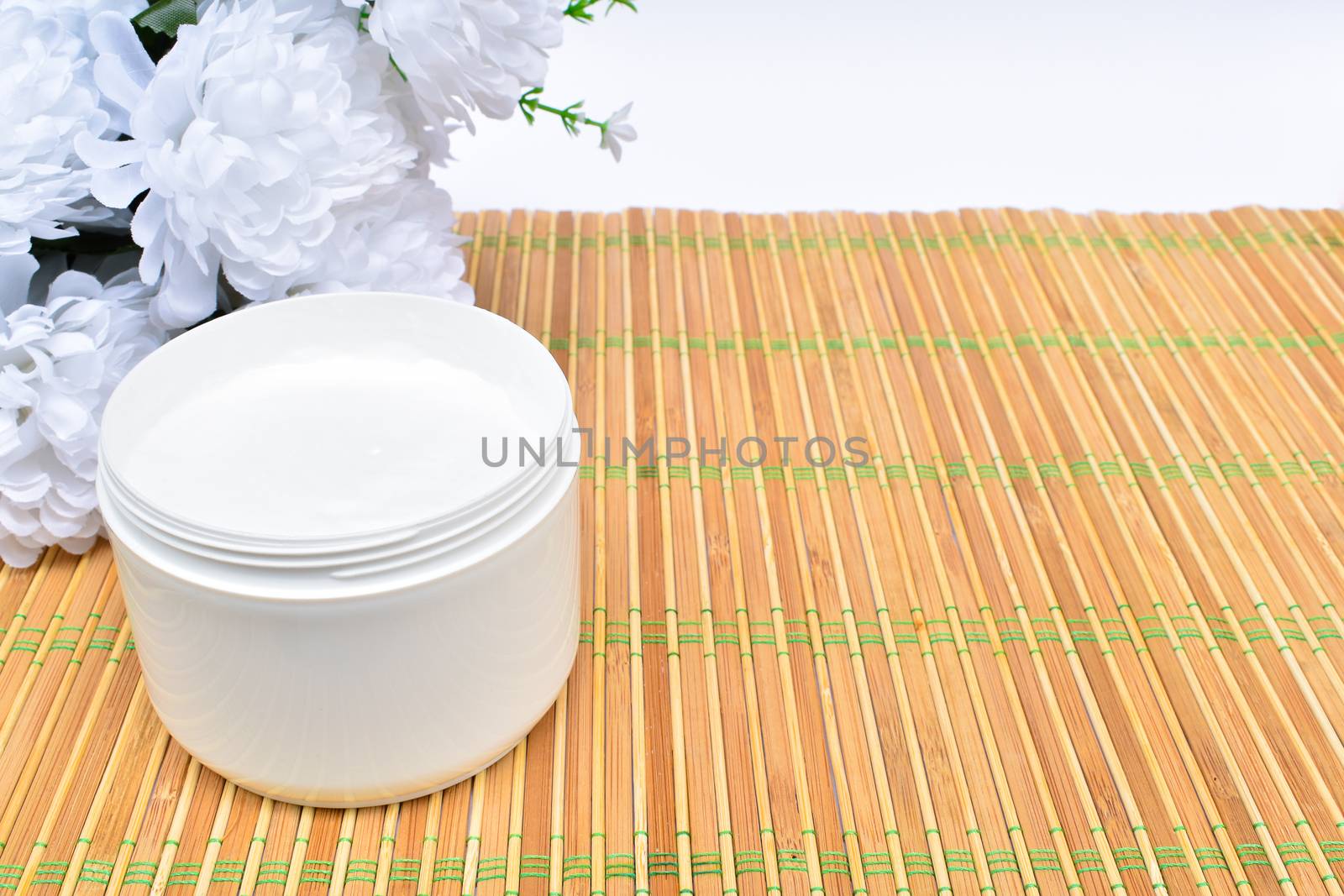 Cosmetic beauty background. White open jar of cream on bamboo washer, in the background flower. An empty copy space.