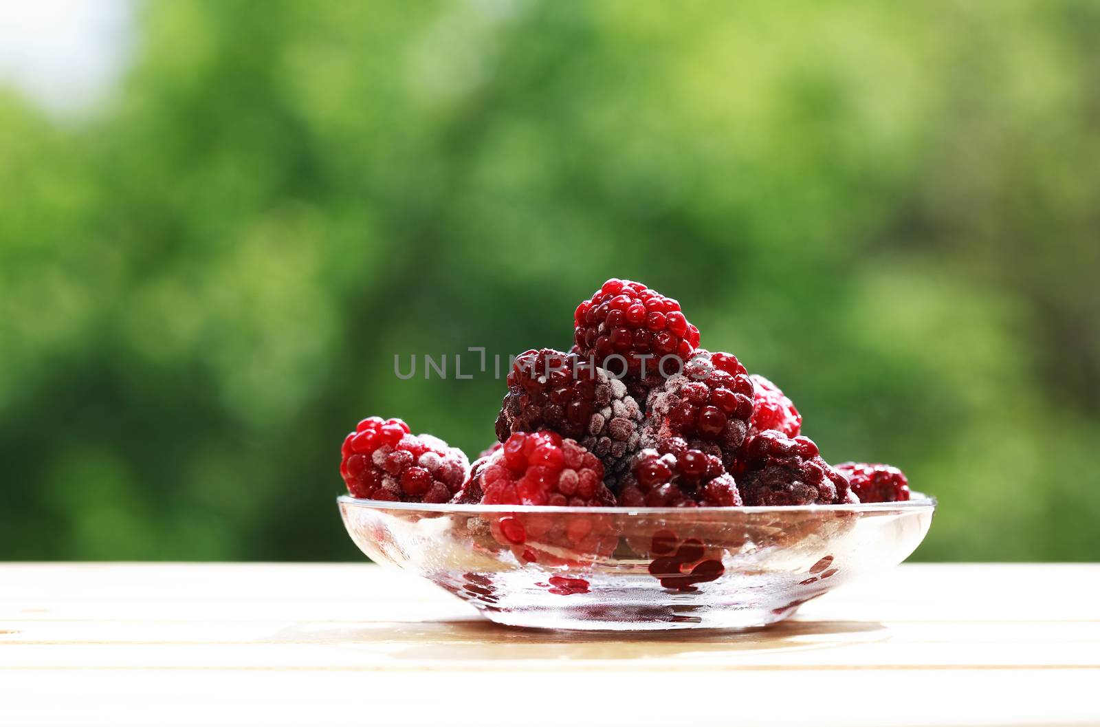 Saucer with heap of frozen blackberry fruits on wood