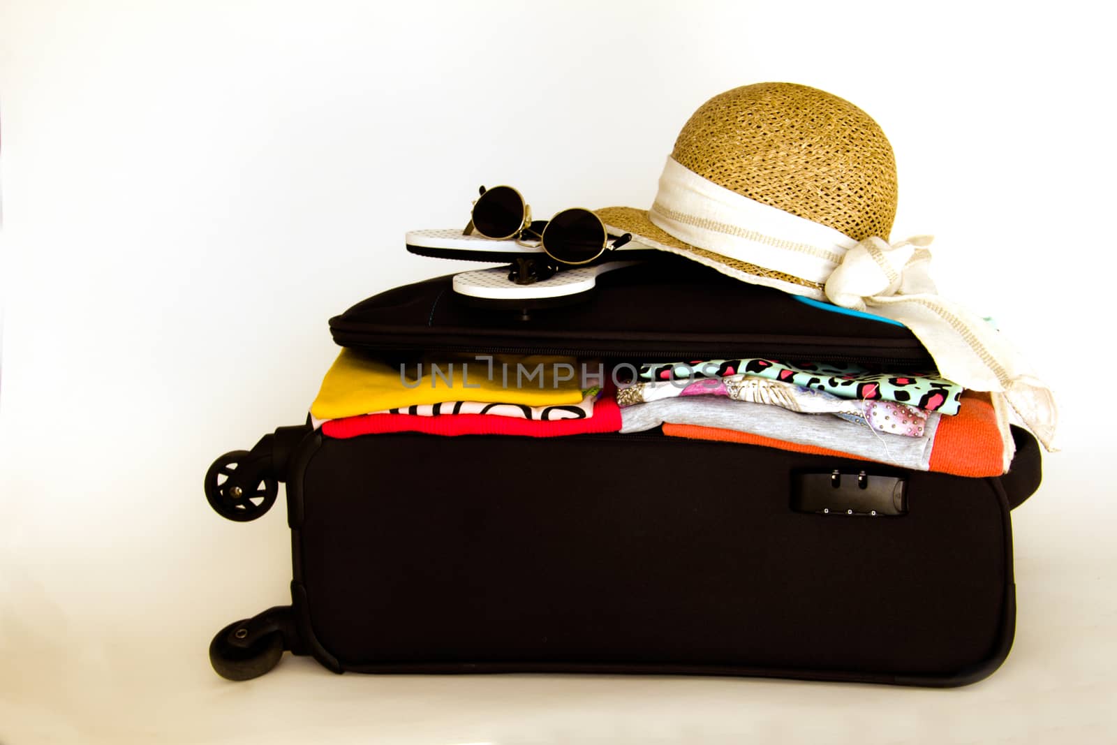opened suitcase containing clothes with sunglasses and a hat on the top