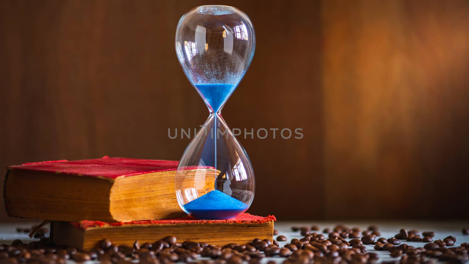 Sand clock on the old book and coffee seed on wooden table. Copy by SaitanSainam