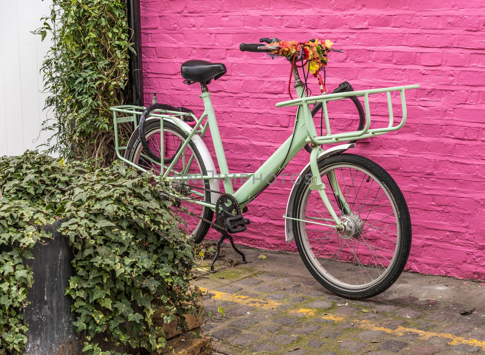 Light green retro, classik bike is parking at a pink wall in a lonely street in London, UK