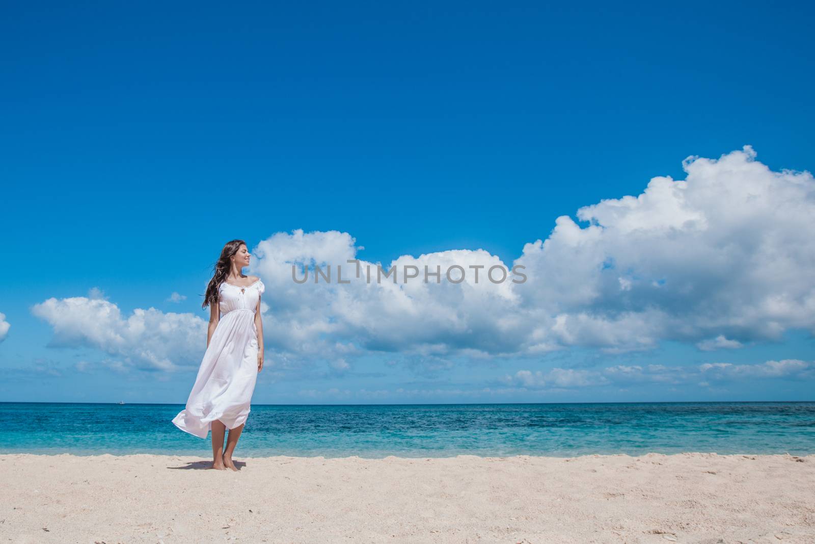 Young woman in white dress walking along sand tropical beach