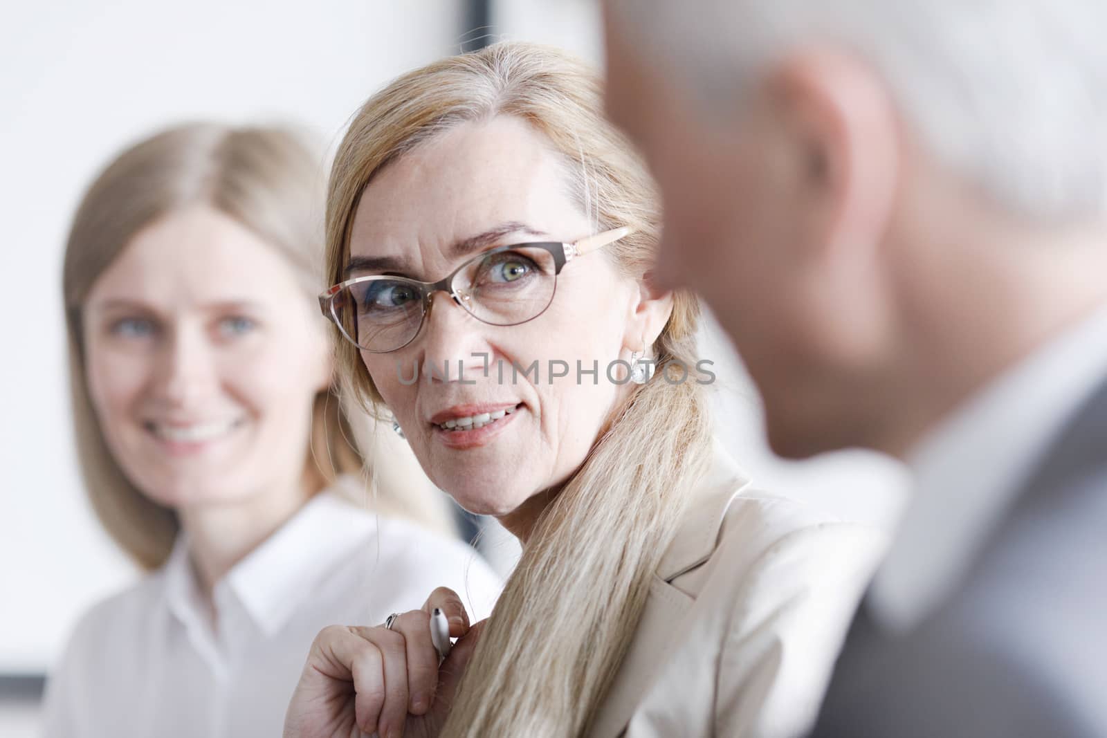 Business people sitting in a row and working, focus on mature woman in glasses