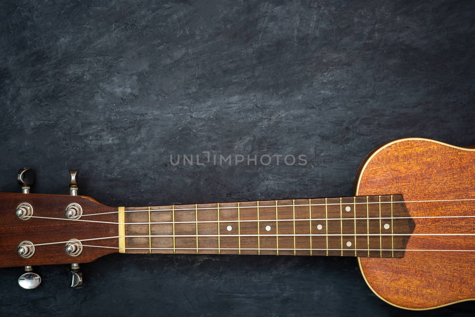 Ukulele on black cement background. Neck and strings of ukulele parts. Copy space for text. Concept of Hawaiian musical instruments and music lovers.